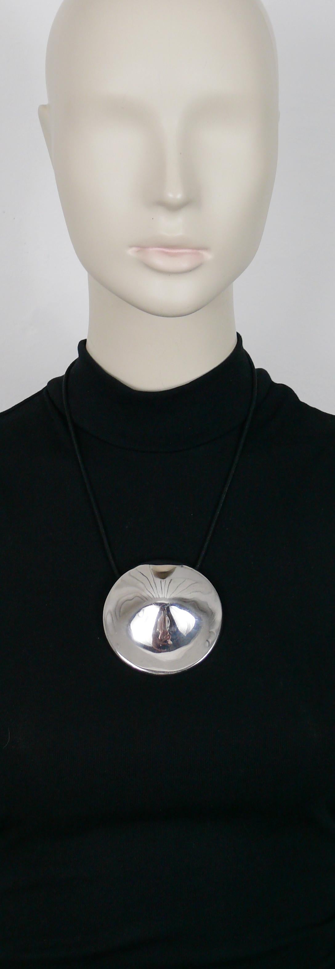 THIERRY MUGLER Anhänger-Halskette mit einer massiven, geschwungenen Scheibe aus Sterlingsilber, die durch eine Politur einen Spiegeleffekt erhält.

Schwarze, schlauchförmige, geflochtene Kordel.

Geprägtes THIERRY MUGLER.
Vollständig gestempelt mit