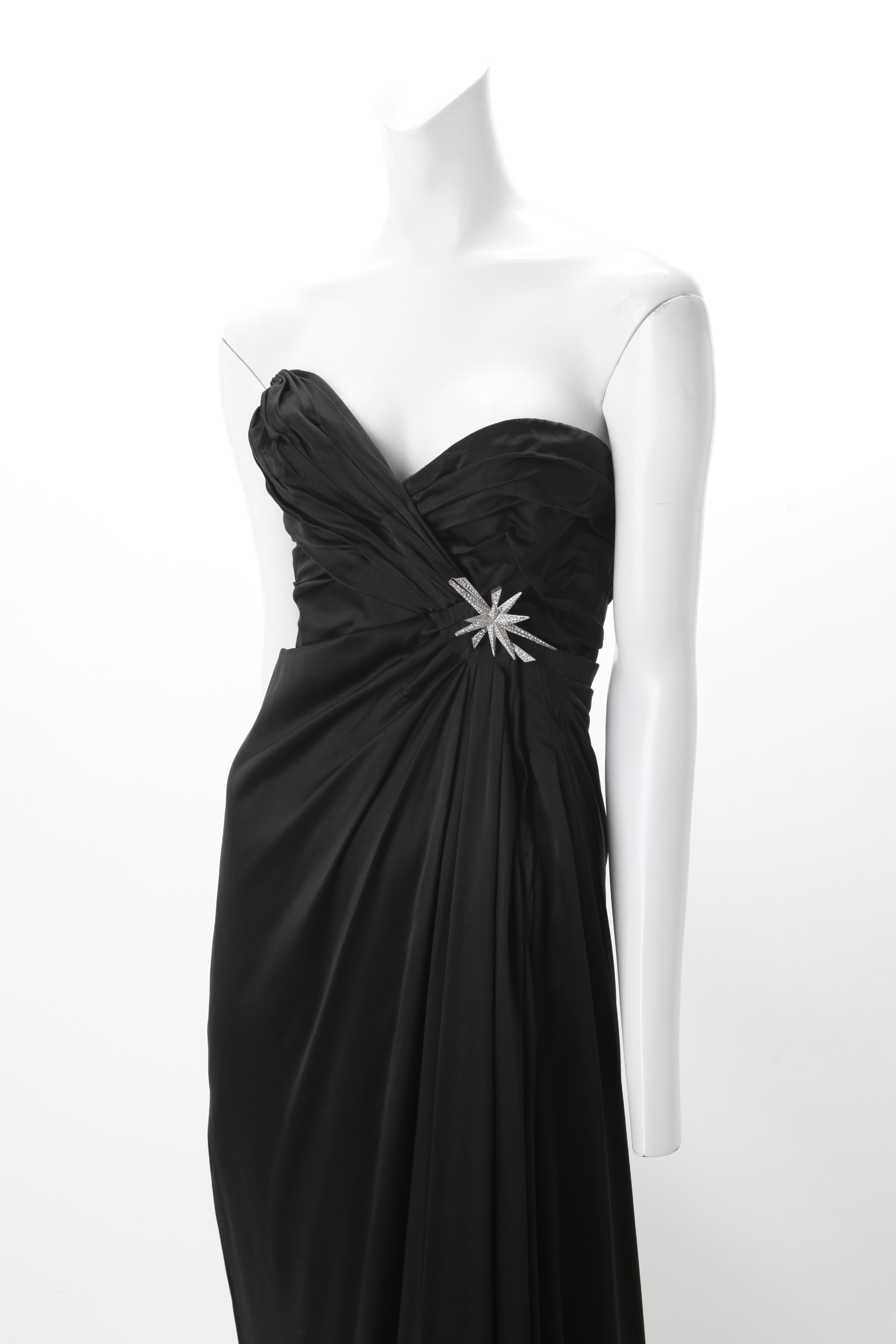 Thierry Mugler Trägerloses Kleid aus schwarzem Satin, ca. 1980er Jahre
Trägerloses Kleid aus schwarzem Satin von Thierry Mugler mit asymmetrischem, gerafftem Korsett und Strassbroschen-Akzent. Der Rock weist geraffte Falten auf, die von einer