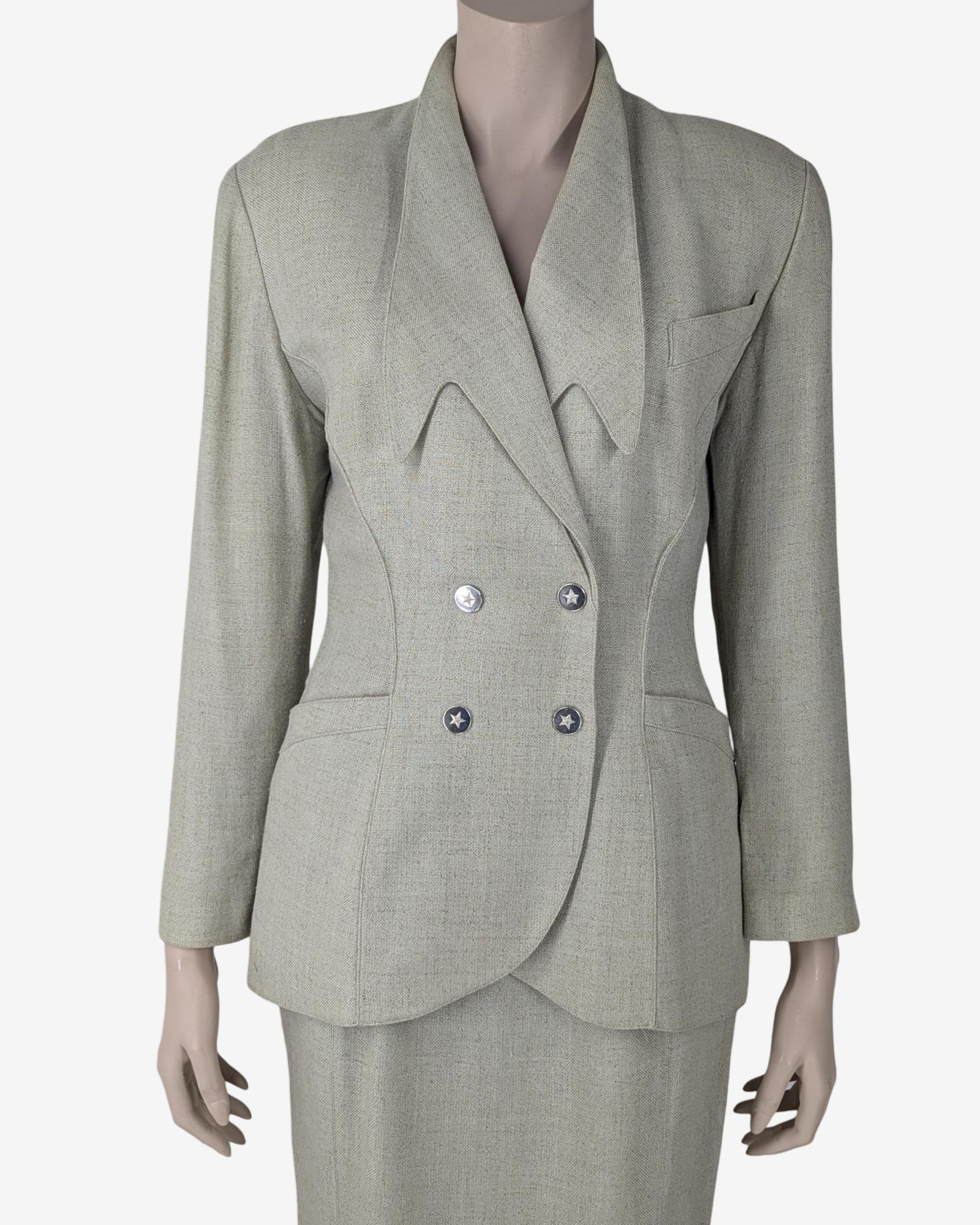 Thierry Mugler Tailor Set Blazer & Rock

Blazer mit langen Ärmeln, die aus 4 Sternchen-Druckknöpfen bestehen, Vorder- und Rückseite mit Ausschnitten, abgerundeter Blazeröffnung, Schultern mit Schulterpolstern, tailliertem Kragen und zwei