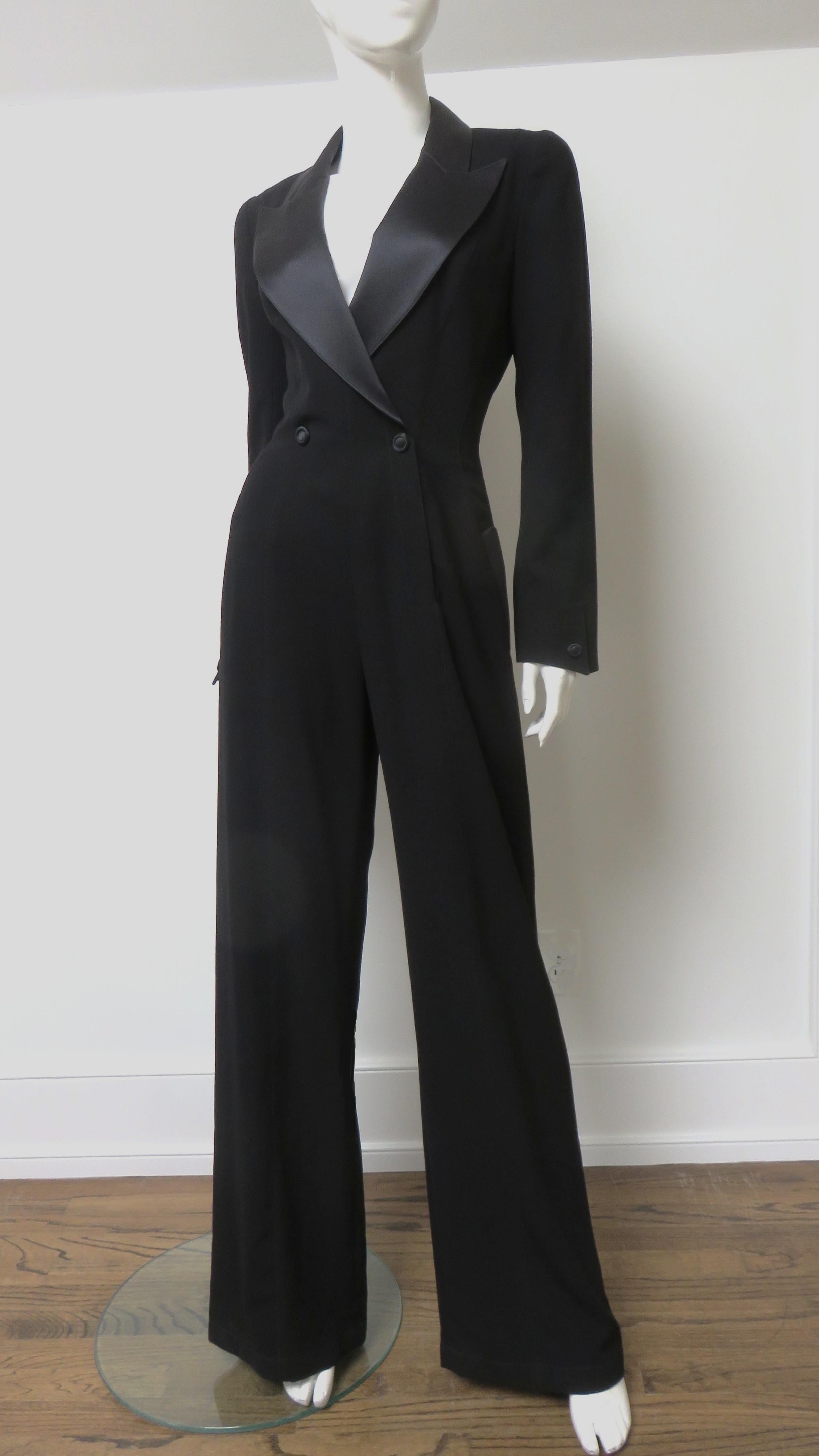 Un fabuloso mono negro de Thierry Mugler.  Tiene influencia de esmoquin con solapas de pico de seda, bolsillos con solapa y broches decorativos que cierran la parte delantera de doble botonadura y uno en cada puño.  Presenta las elaboradas costuras