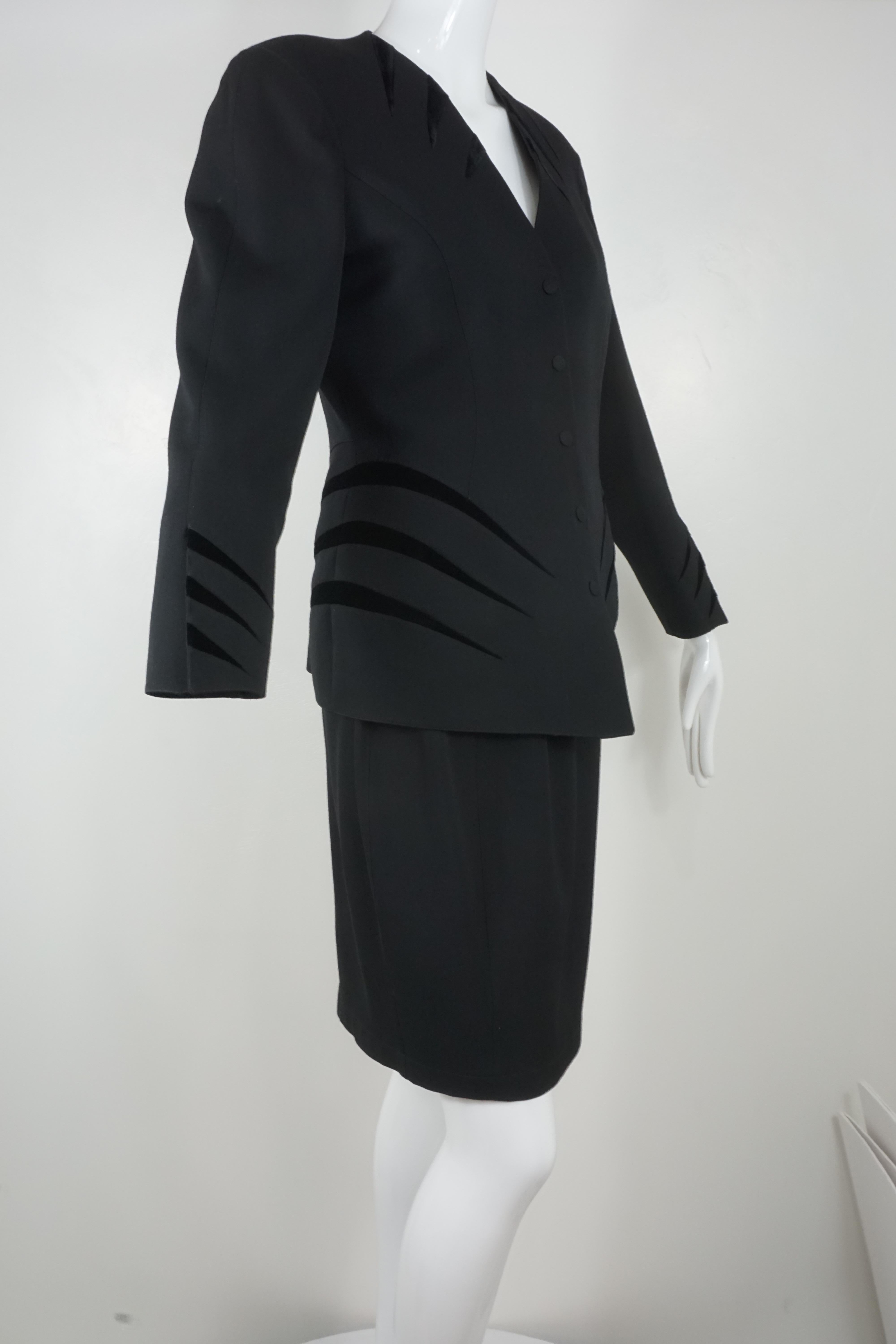 Thierry Mugler vintage suit from the 1990's in black wool with black velvet detailing to accentuate the nipped waist and hourglass figure. Jacket showcases black velvet detailing at the collar, hips and cuffs with a v-cut neckline and five snap
