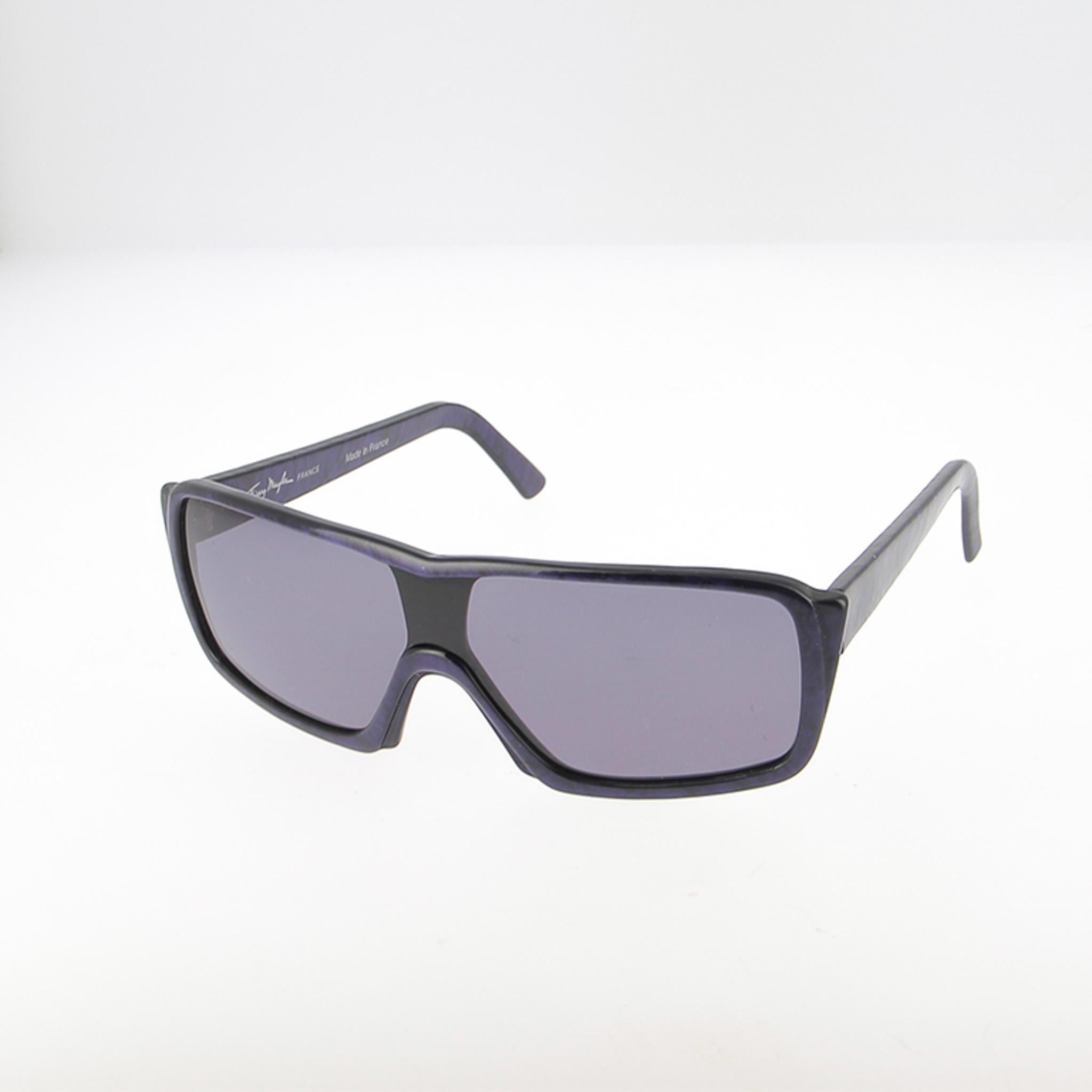 Descubre estas gafas de sol vintage Thierry Mugler, un modelo emblemático de los años 90 que destila el espíritu futurista y de alta costura de la casa. La montura de estilo máscara adopta una silueta envolvente, un único barrido continuo de sien a