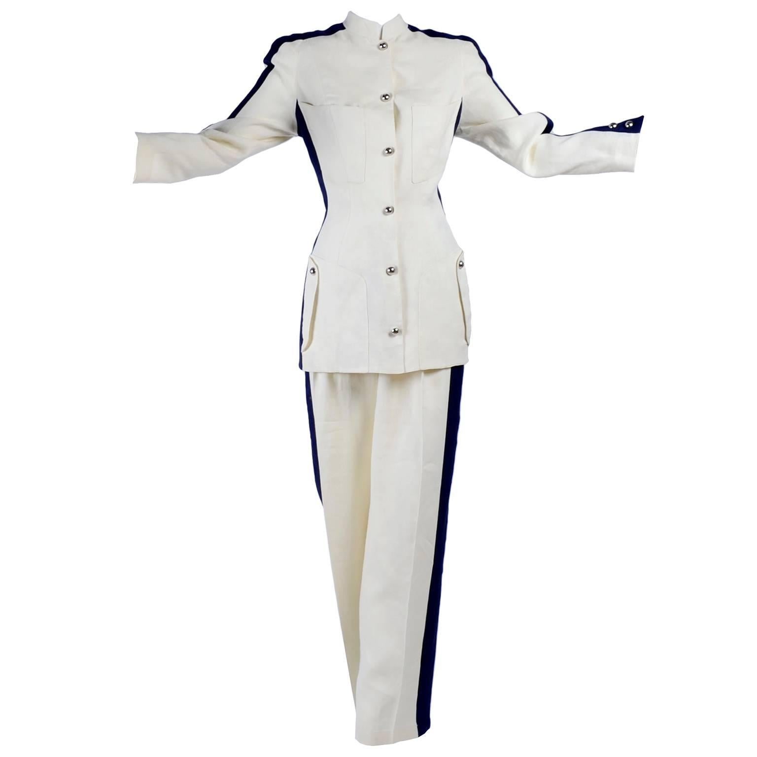 This is a fabulous 2 piece lighter weight linen blend pant suit designed by Thierry Mugler that includes a pair of high waist trousers and a long jacket. Both the jacket and pants have wide tuxedo style navy blue stripes up the side. The jacket is