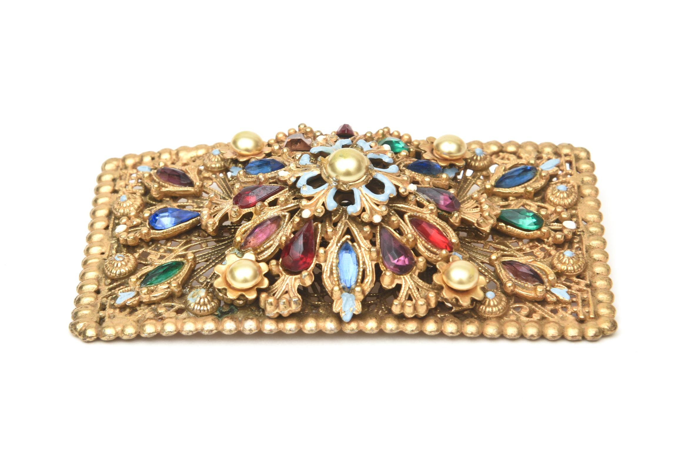 This stunning and amazing pin made for the Thieves of Baghad movie is encrusted with vibrant color and ornate details. it is square with colored glass in varying forms, enamel and faux pearl. It is hallmarked Thieves of Baghad. It is gold plated and