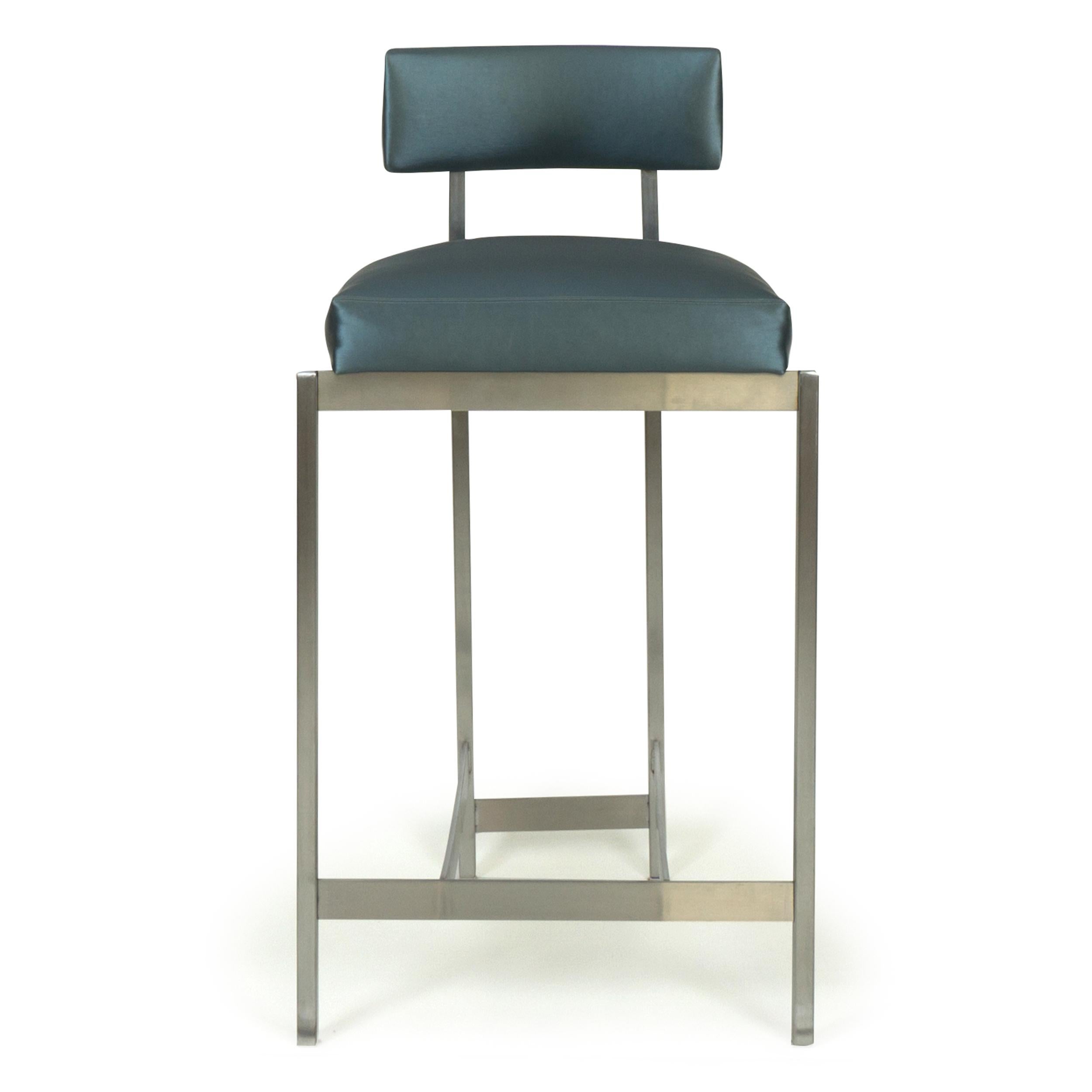 Inspired by Italian design, this stool can be made for bar or counter height. Stretched, elongated lines of the brushed stainless steel base are juxtaposed against a broad, squat seat and back covered in a durable Romo gray metallic vinyl. Seat