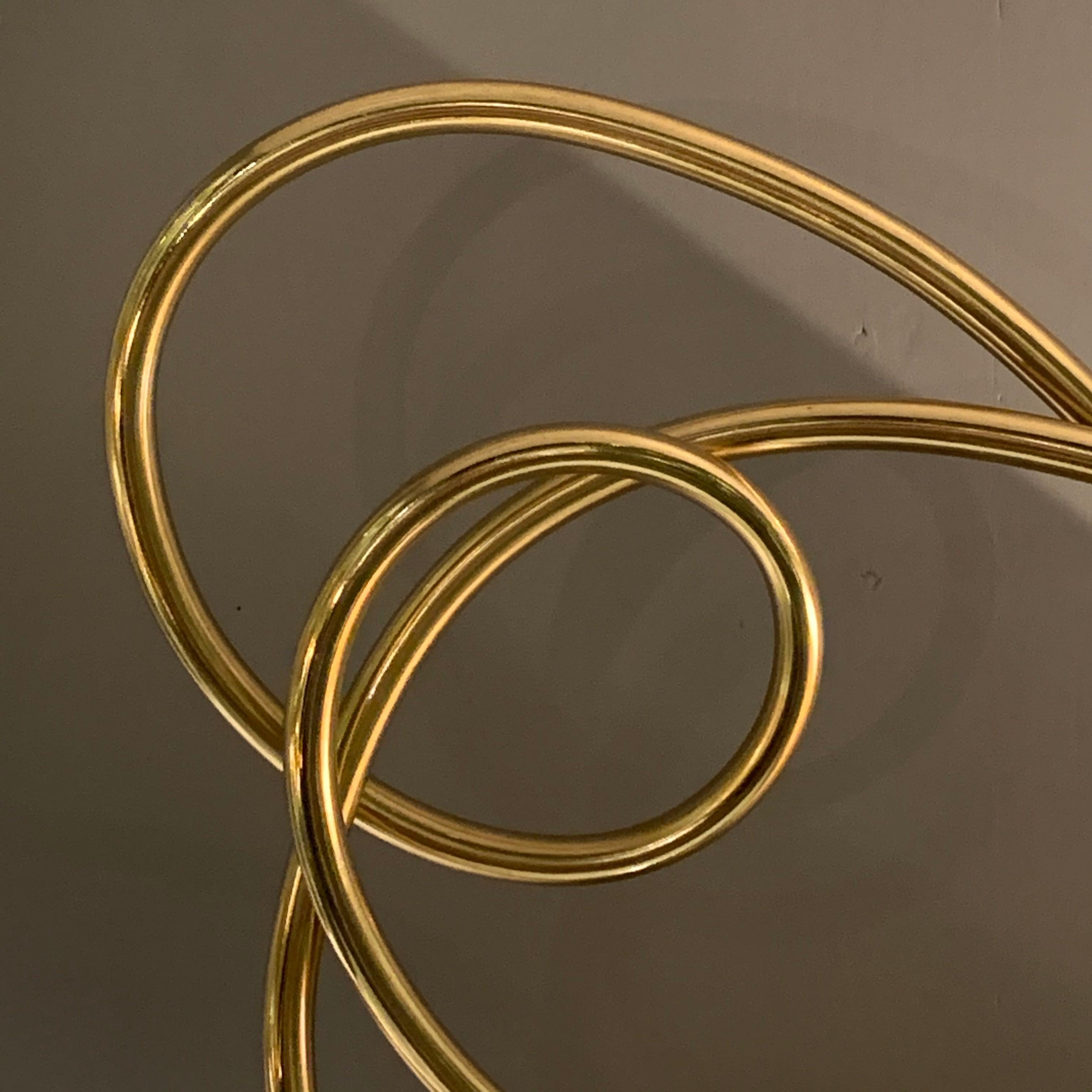 The free form thin ribbon shaped brass curves around to form multiple circles.
The sculpture is mounted on a black marble base.
The base measures 3.5