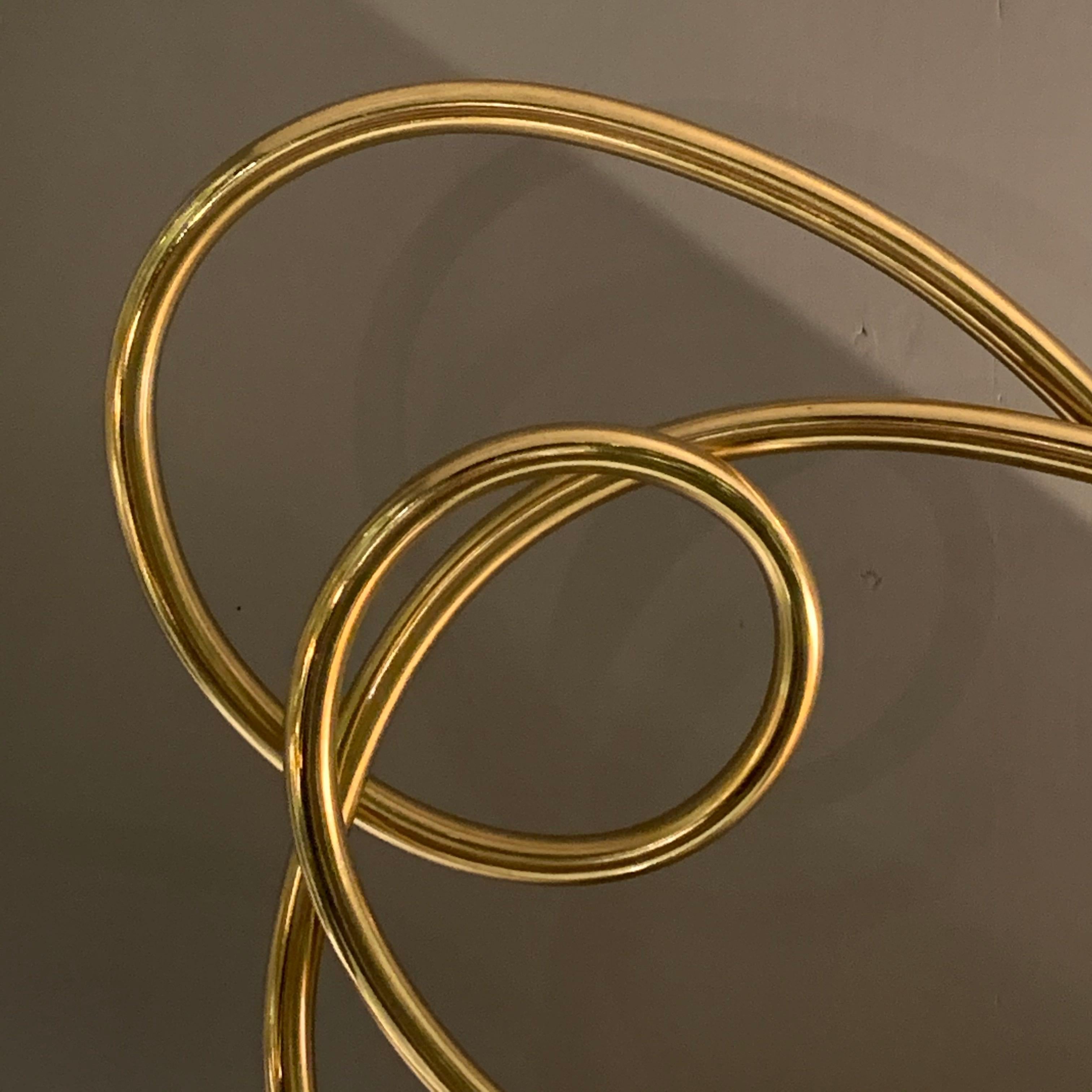 Le laiton en forme de ruban fin et libre s'incurve pour former de multiples cercles.
La sculpture est montée sur un socle en marbre noir.
La base mesure 3,5