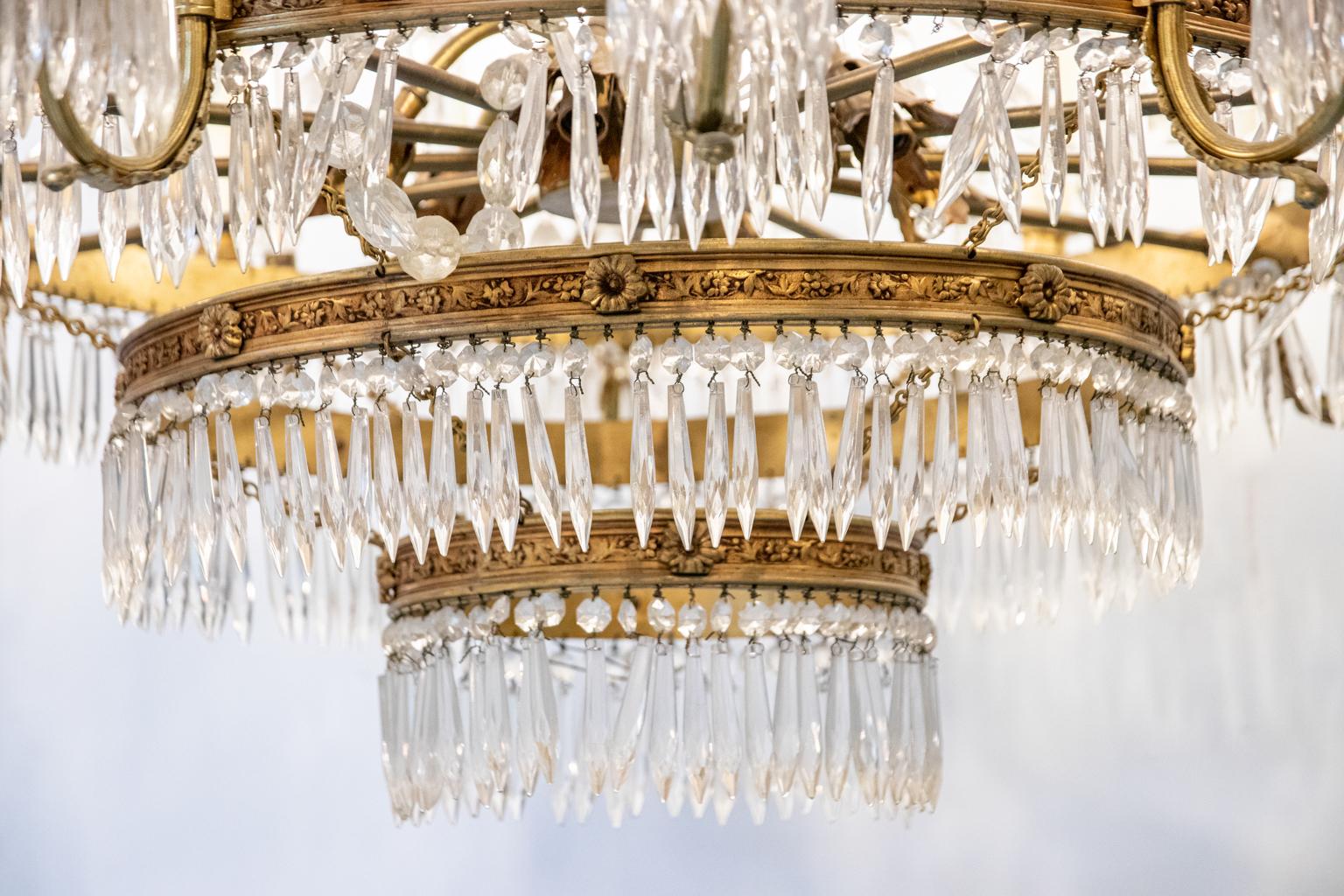 Thirteen arm crystal and bronze three tier chandelier with pendant pointed rectangular prisms and beaded strands of crystal. The piece further detailed with a scrolled acanthus leaves on the top of the chandelier, pointed spear shaped crystal