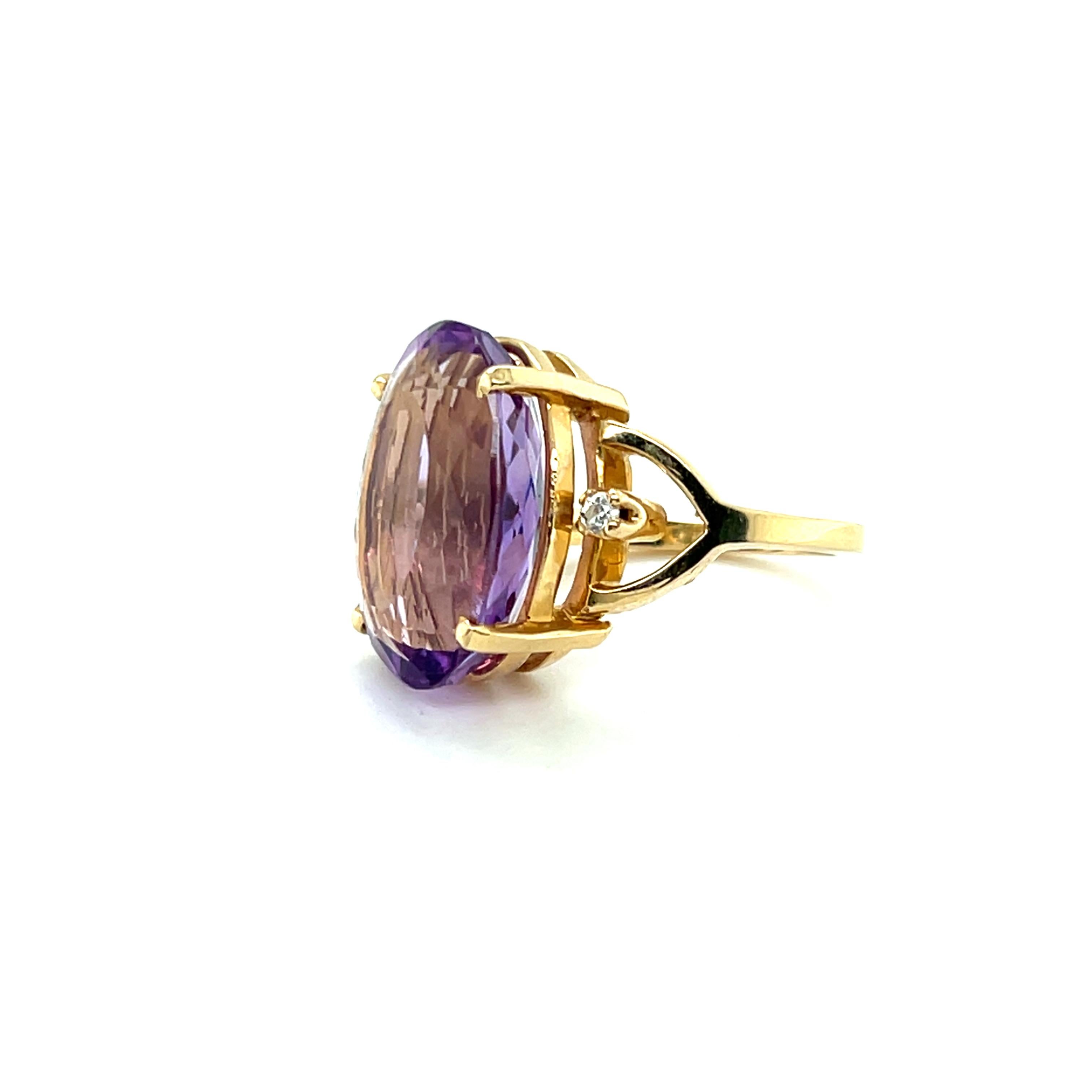 This contemporary 14 karat yellow gold ring features a striking oval-cut amethyst weighing approximately 12.71 carats. The vivid purple gemstone is beautifully complemented by two round brilliant accent diamonds totaling approximately 0.05 carats,