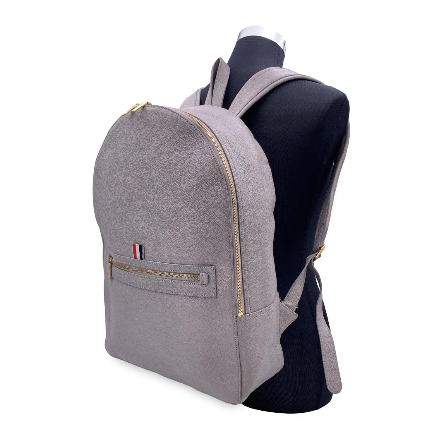 Thom Browne Classic Backpack Bag in Grey Pebble Grain leather. It features a tricolor Grosgrain loop tab and designer's signature in gold metal on the front. Single top handle, double adjustable back straps. Zip around closure. 1 zipper pocket on