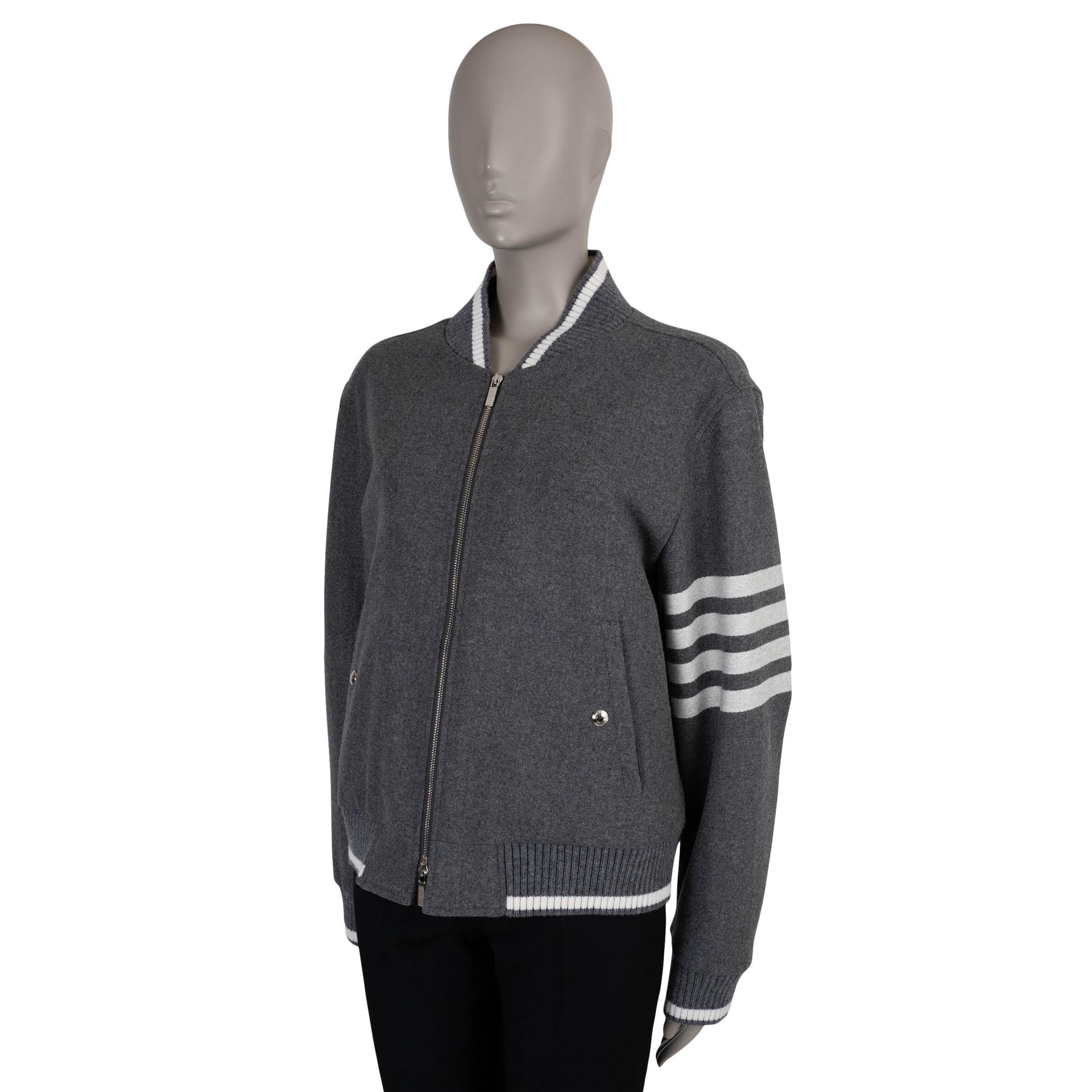 This 100% authentic Thom Browne bomber in medium grey flannel wool (95%) and cashmere (5%) offers a refined take on a classic silhouette. Designed with a cropped fit, it features the signature white three stripes on the sleeve, buttoned pockets at
