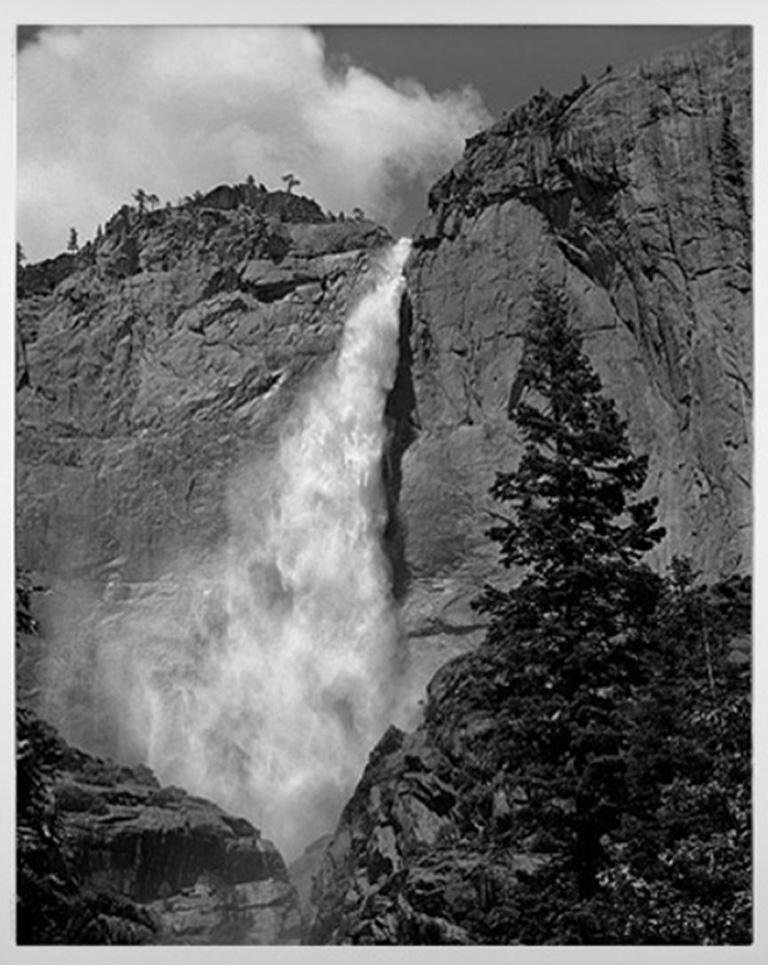 "Yosemite Falls" est une photographie en noir et blanc signée par Thomas Ferderbar. Cette vue de la cascade est une vue latérale et non centrale. On peut voir à quel point l'eau tombe et où elle crée de la brume. Un arbre à feuilles persistantes