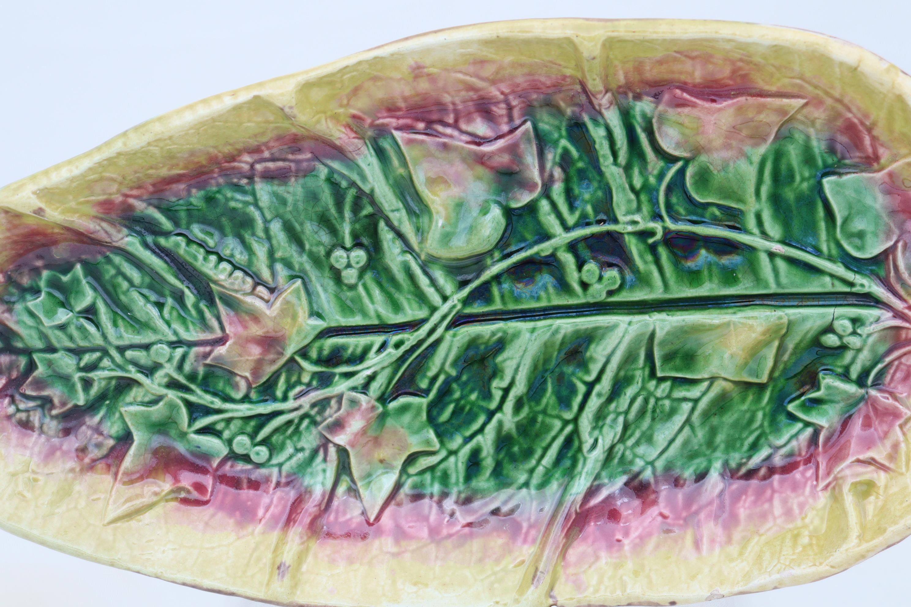 This majolica serving tray by Thomas Forester is modelled as a large leaf overlaid with a strand of ivy leaves and seeds which runs down its length, and coloured with green, magenta and yellow glazes. It measures 340 mm (13.25 inches) in length, 190
