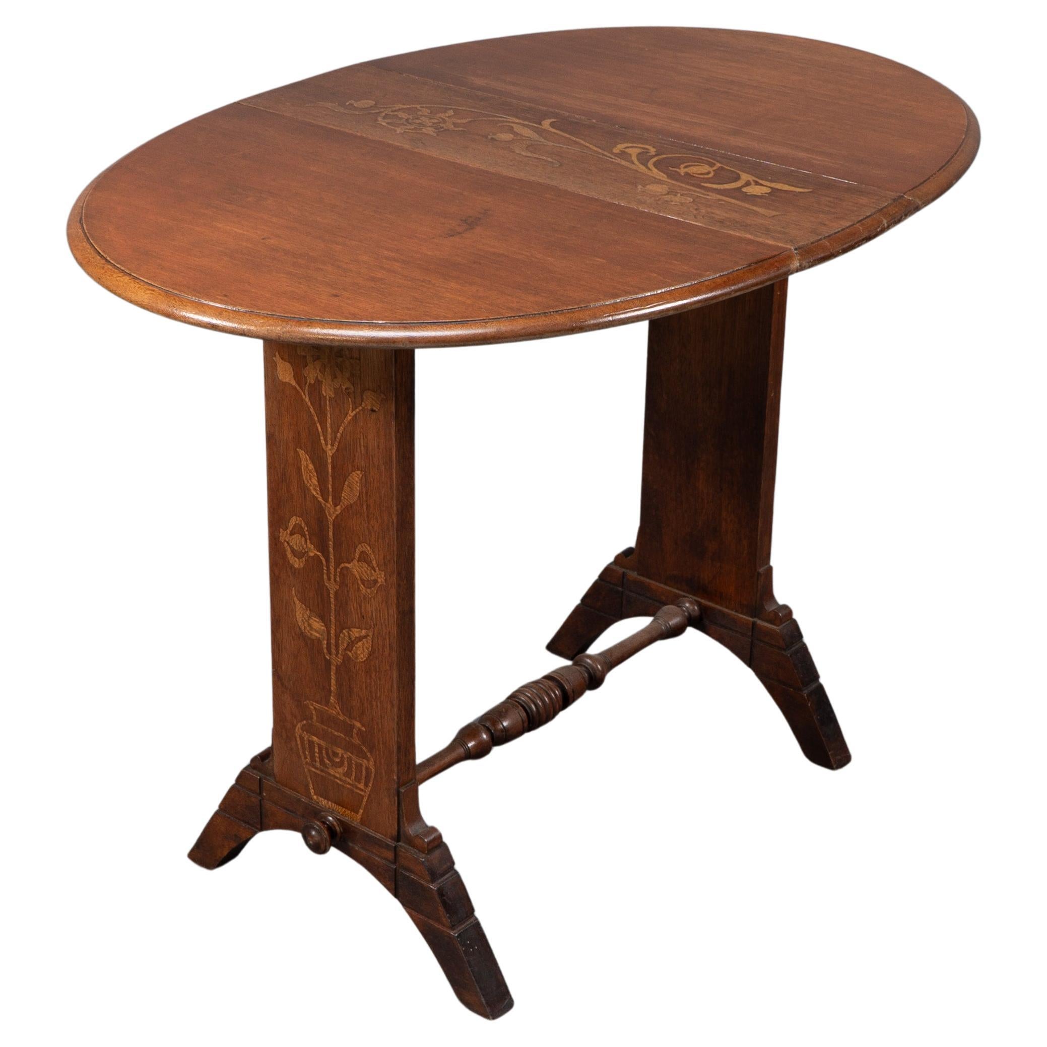 Thomas Jeckyll atribuido. Sutil mesa auxiliar de roble de estilo anglojaponés con hojas abatibles. El tablero oval tiene incrustaciones de una flor en el panel central y una flor que sale de una jardinera de estilo japonés a ambos lados. Los pies,