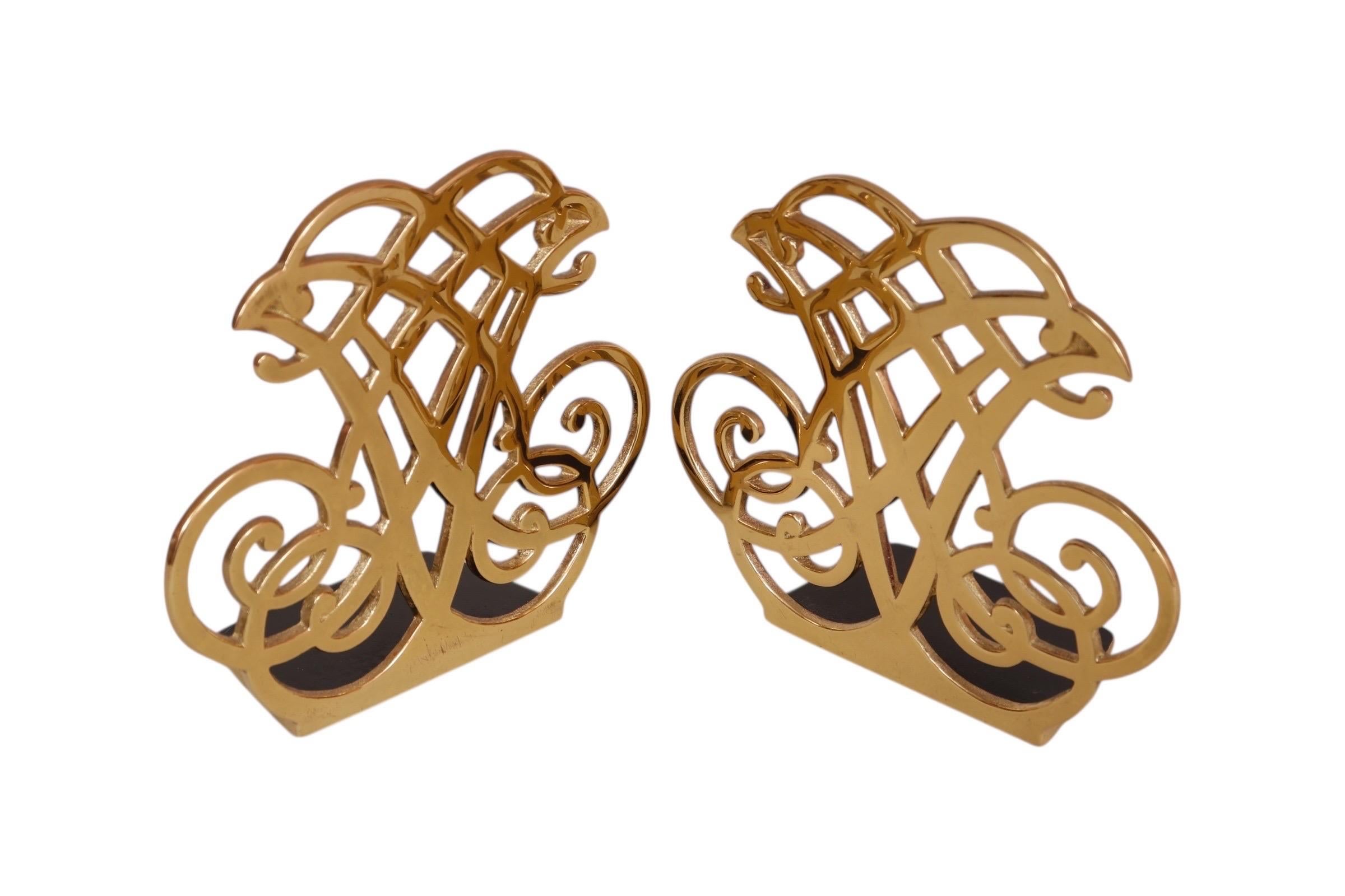 Paire de serre-livres en laiton à volutes fabriqués par Virginia Metalcrafters pour leur collection Thomas Jefferson Cipher. Les serre-livres sont moulés avec un monogramme calligraphique et portent au dos le titre, le copyright de 1987 et la marque