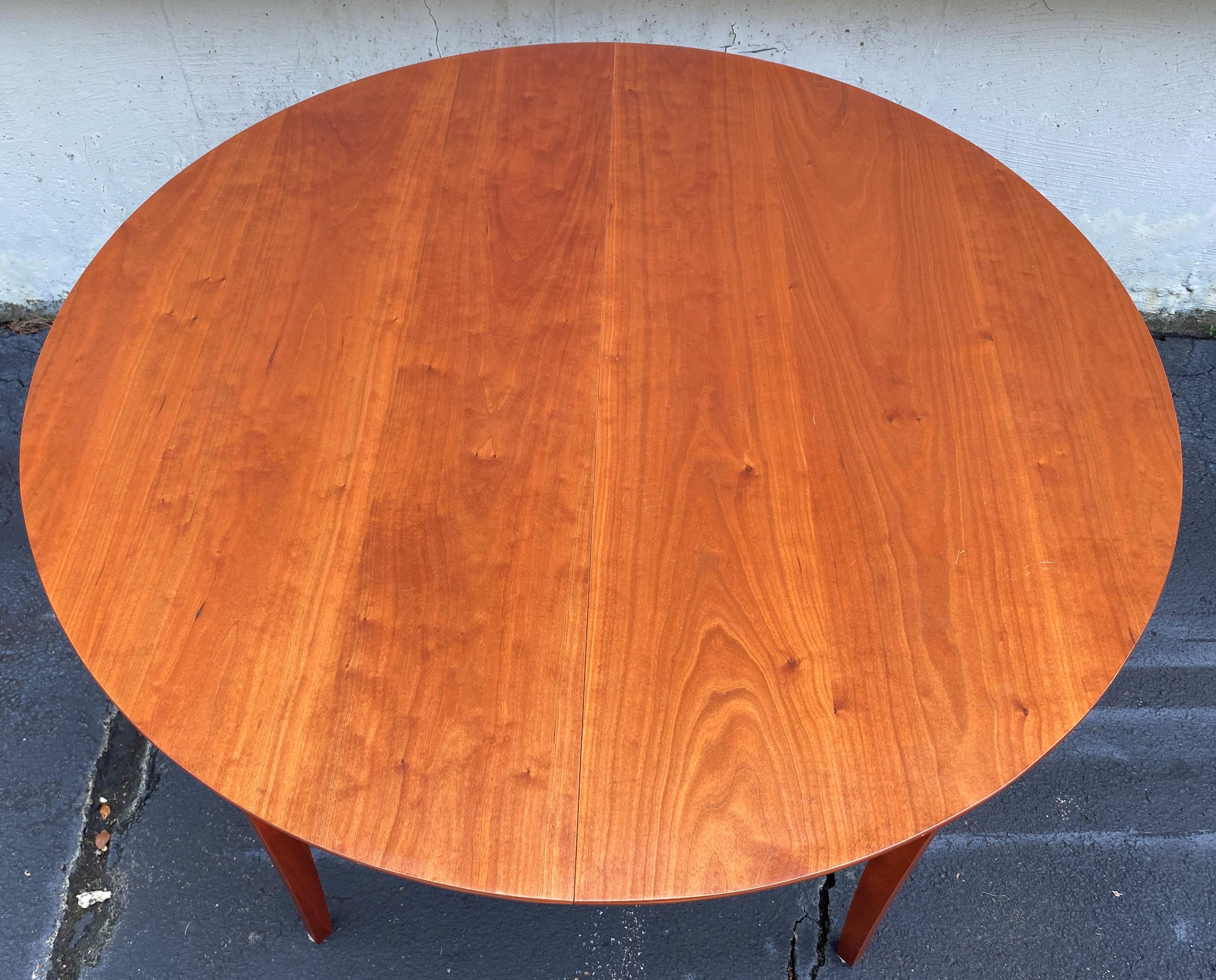 A fine handcrafted round cherry dining table or center table that will expand for a single locking 22 inch finished leaf (with storage bag), supported by four tapered square Hepplewhite style legs. Thomas Moser Handmade American Furniture is based