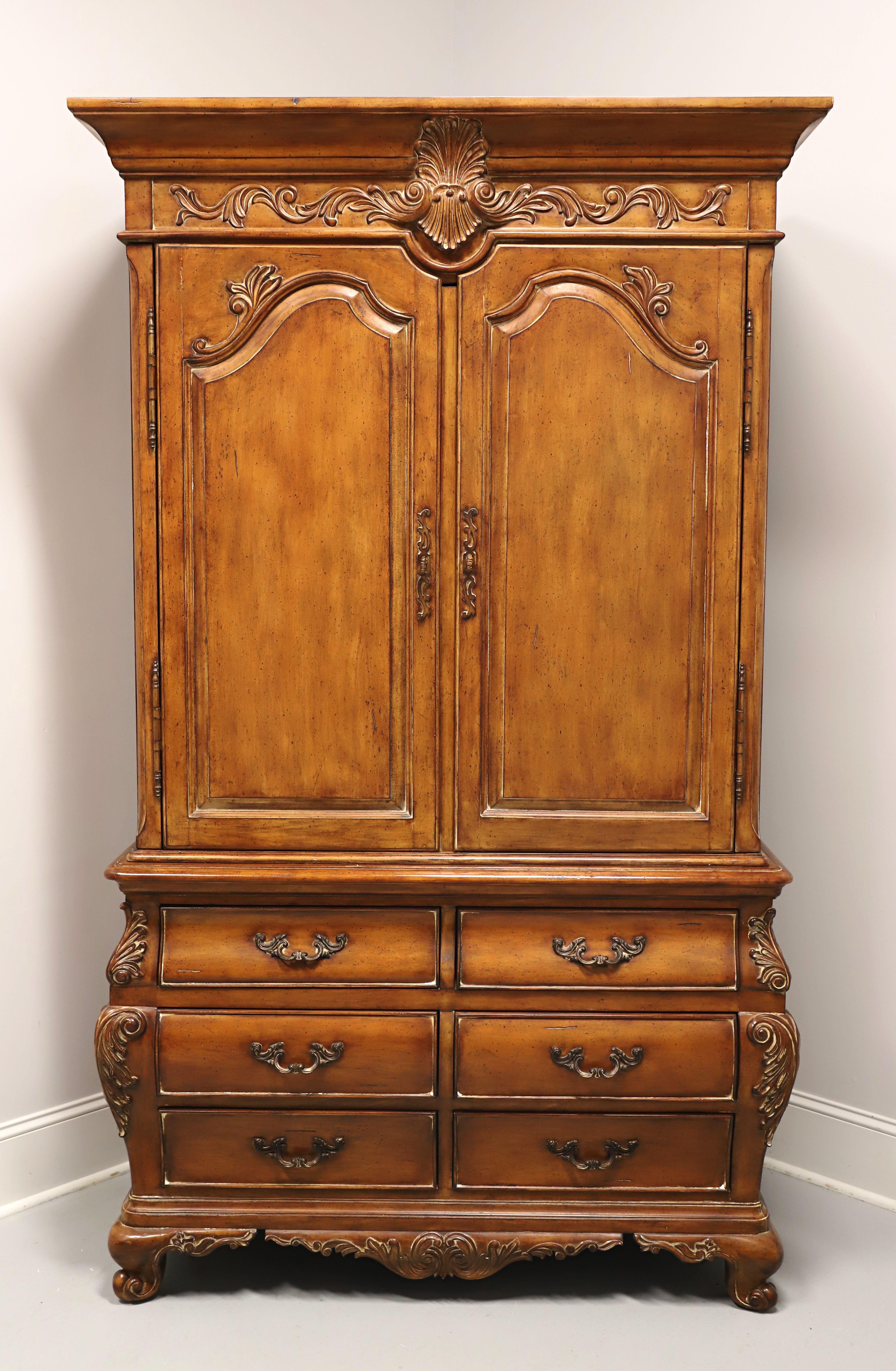 An armoire / linen press in the French Country style by Thomasville, from their Chateau Provence Collection. Walnut with brass hardware, a slightly distressed finish, crown molding to the top, decorative carving to the frieze above the doors,