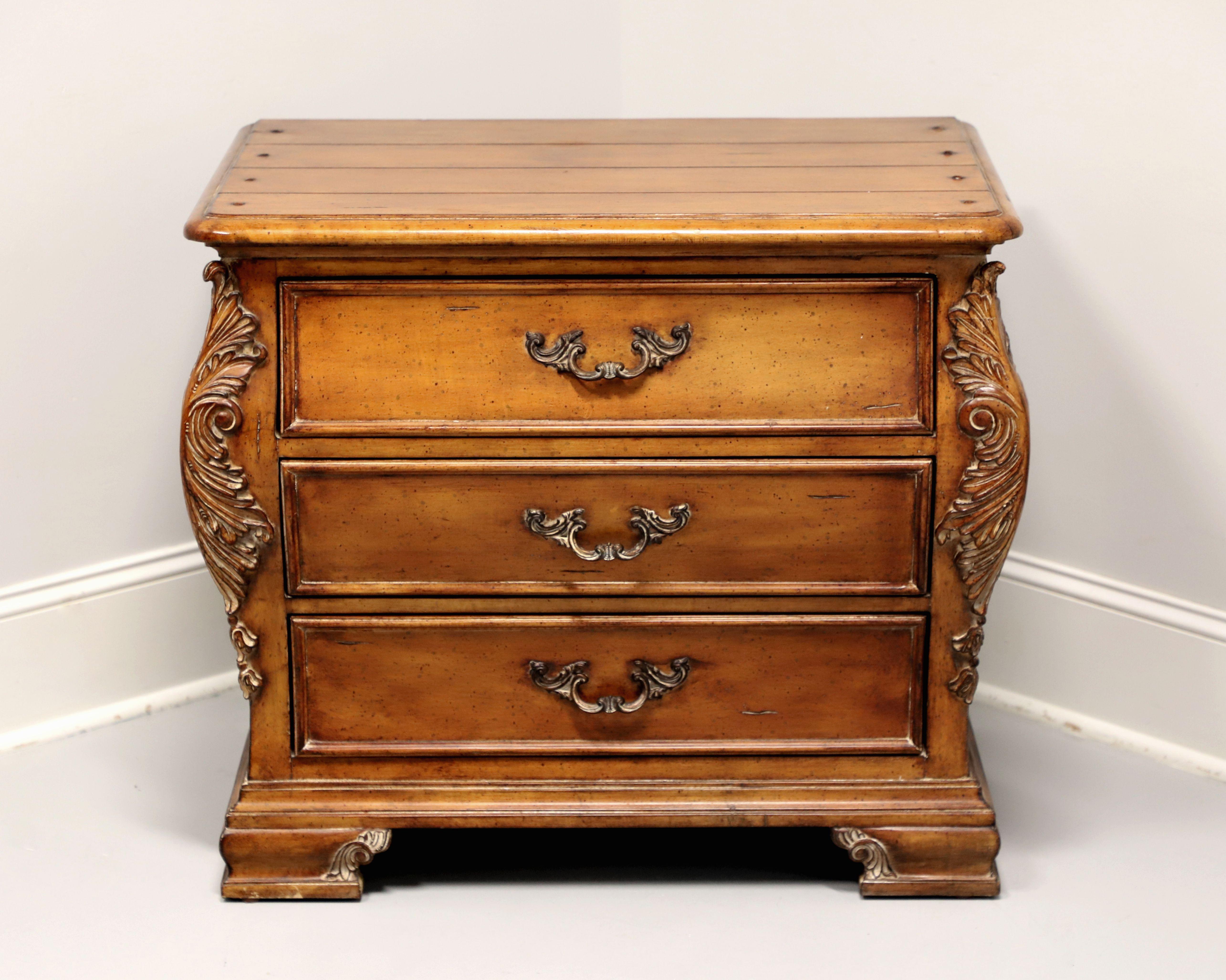 A bedside chest in the French Country style by Thomasville, from their Chateau Provence Collection. Walnut with brass hardware, a slightly distressed finish, plank style top with bullnose edge, decoratively carved contoured sides with acanthus