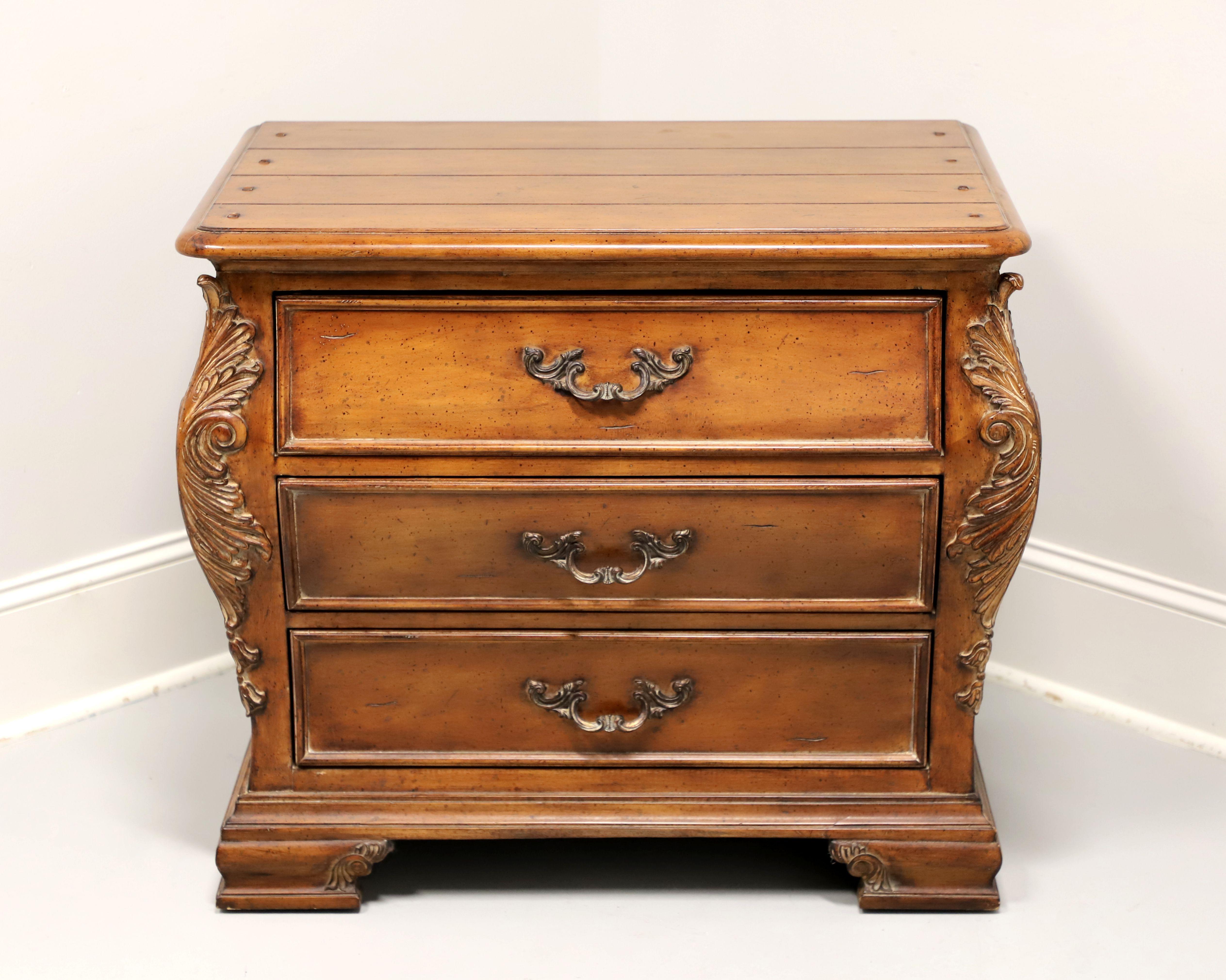 A bedside chest in the French Country style by Thomasville, from their Chateau Provence Collection. Walnut with brass hardware, a slightly distressed finish, plank style top with bullnose edge, decoratively carved contoured sides with acanthus