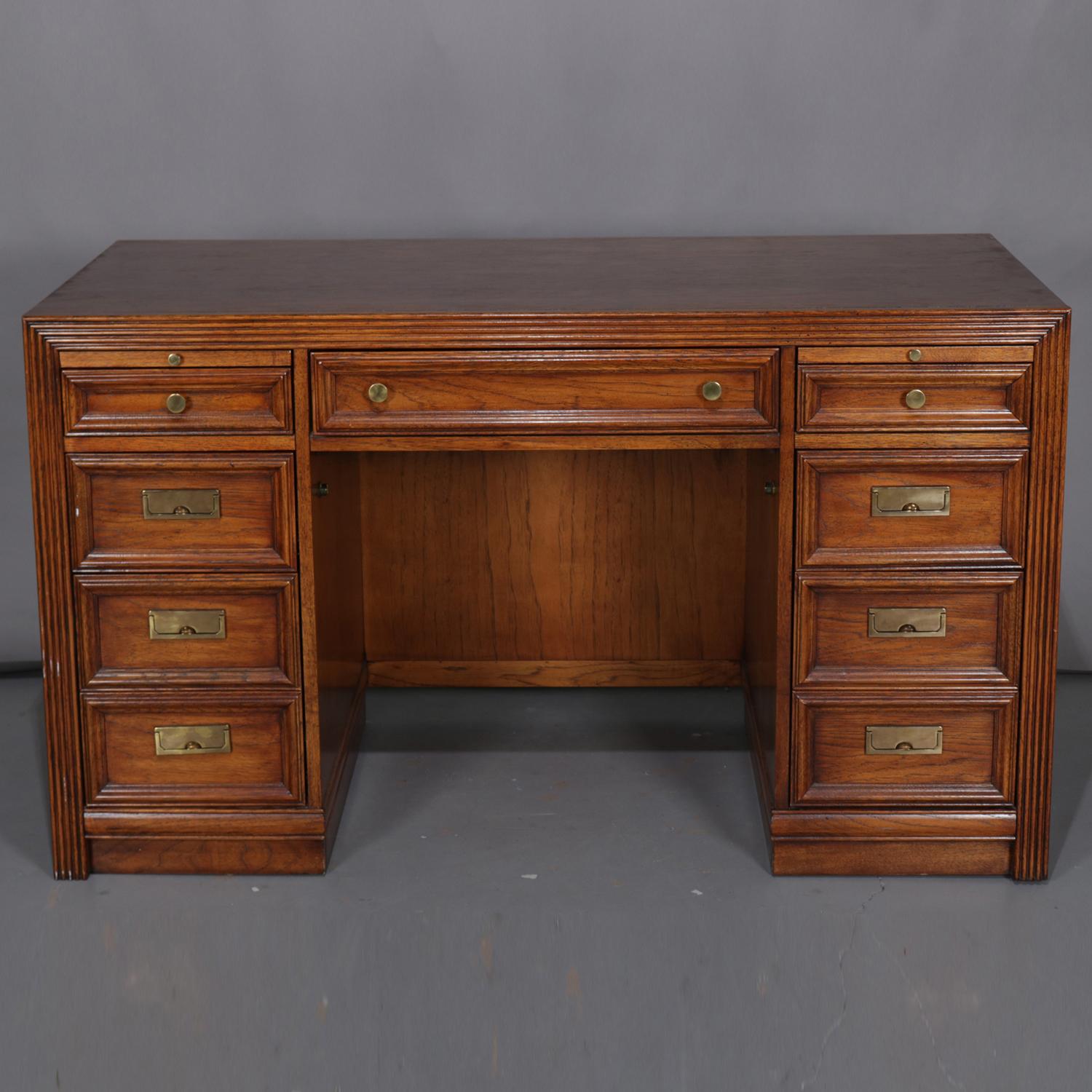 Vintage Campaign desk by Thomasville features oak construction with central long drawer flanked by side columns each having pull-out tray over three graduated drawers, the bottom for files, protective glass included but not photographed, Thomasville