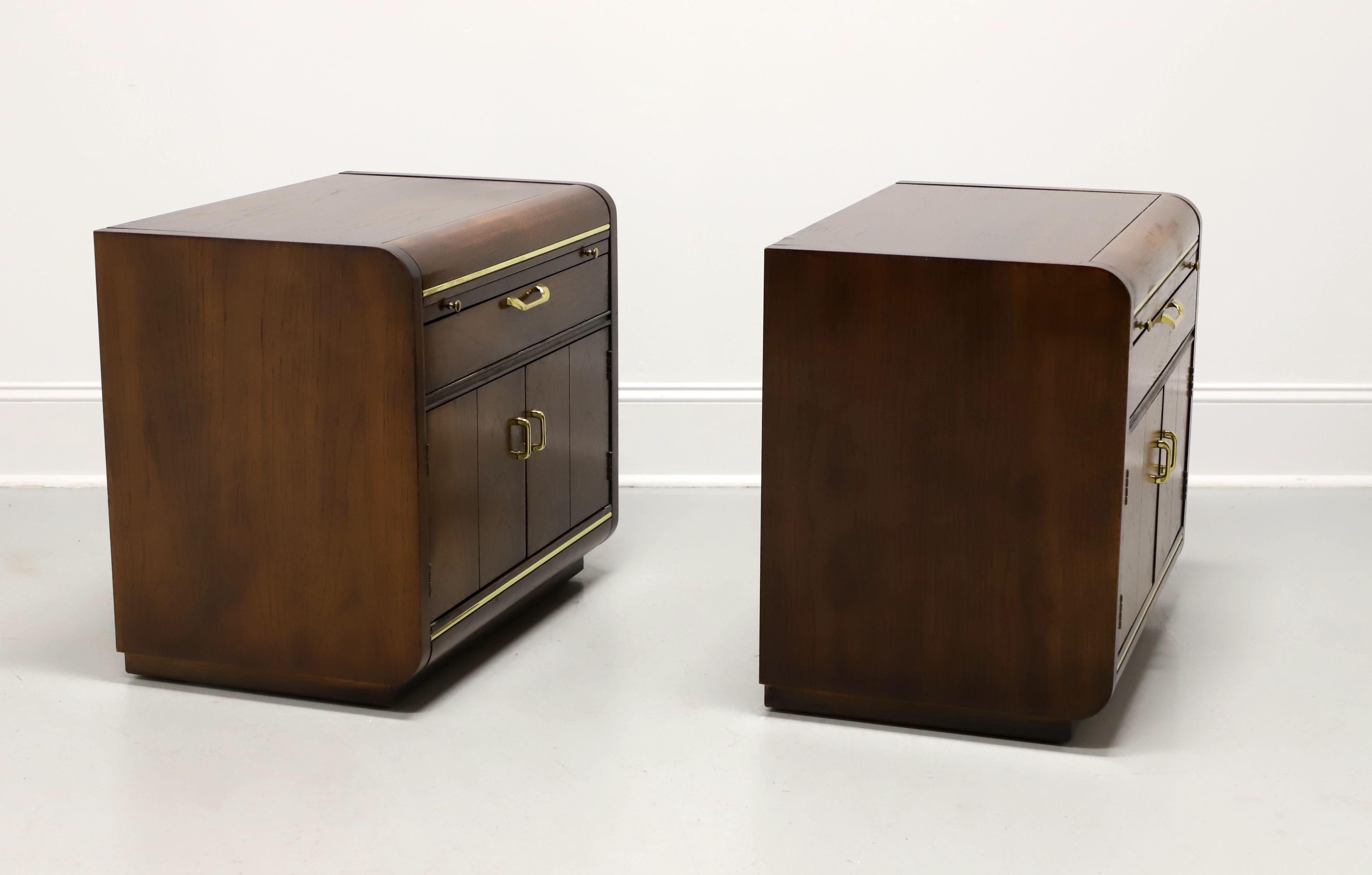 A pair of Post-Modern style nightstands by Thomasville, from their Founders Collection. Walnut with brass hardware & accents, waterfall edges, and on a slightly recessed solid base. Features a pull-out brushing slide, one drawer of dovetail