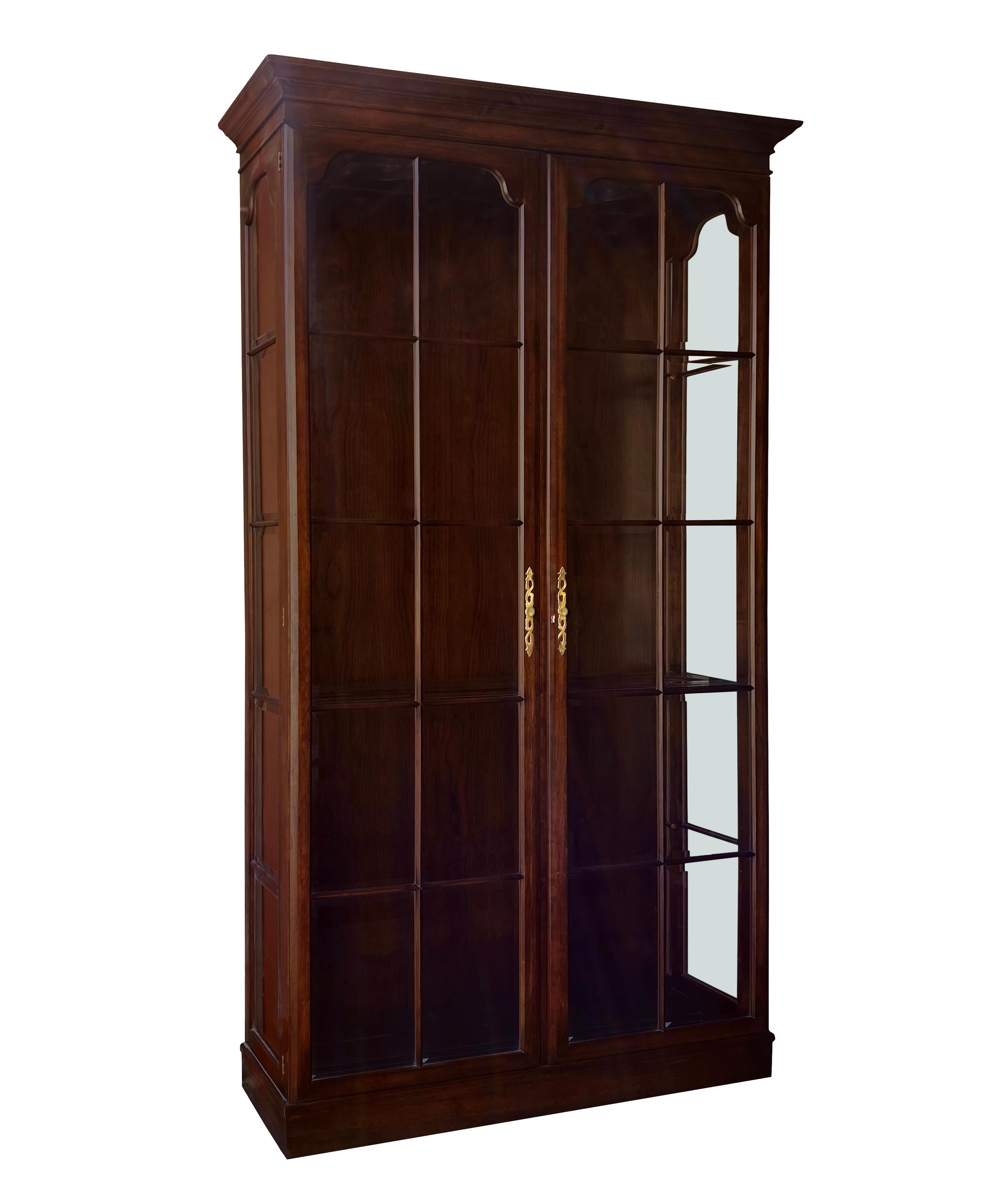 A Thomasville Furniture Collectors Cherry collection display cabinet with brass hardware and glass shelves. Piece has wiring for two recessed lights above and a plug. Piece is in good condition. Note that in two of the photos, the knobs have not