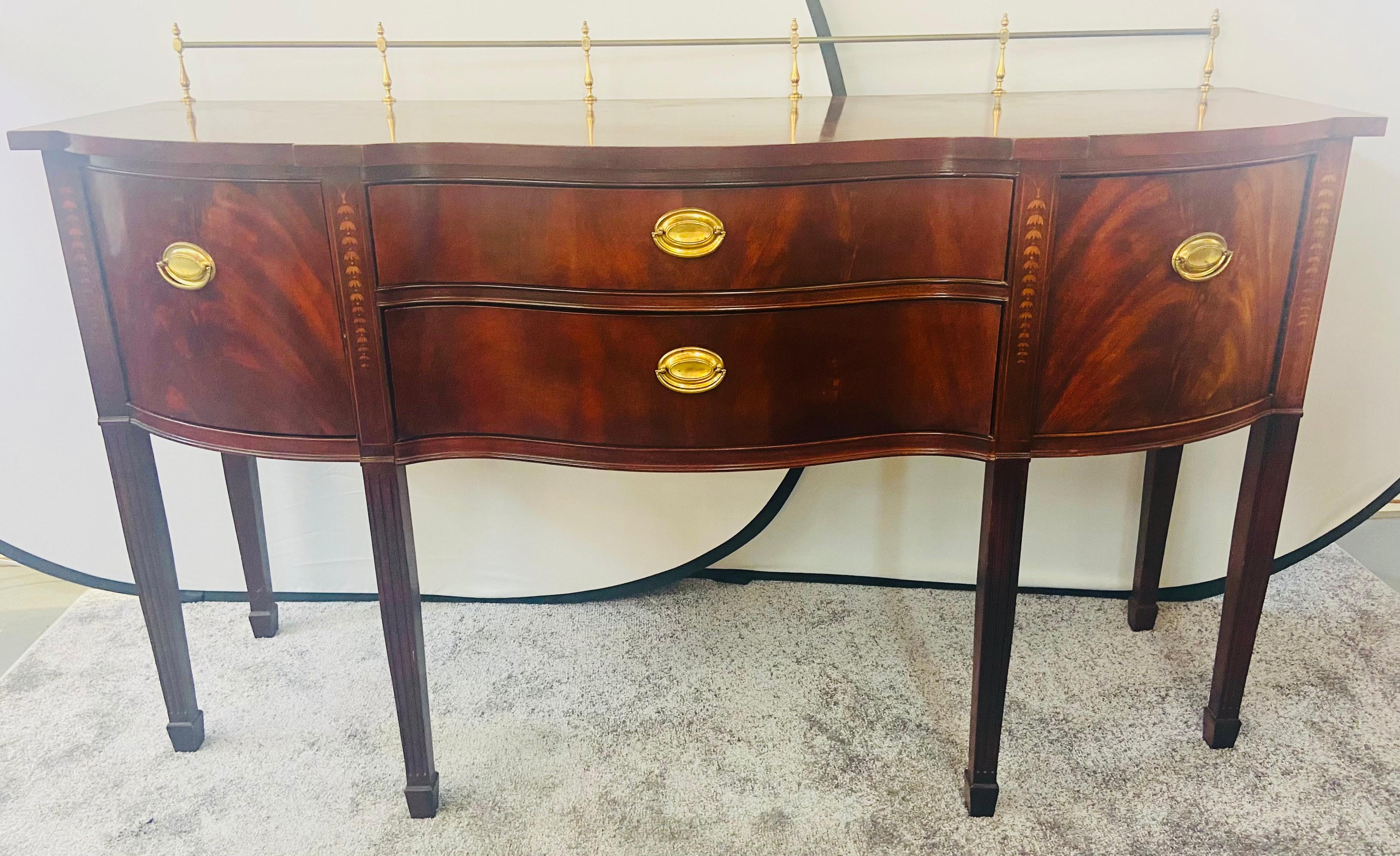 A classical vintage Thomasville Hepplewhite style sideboard or buffet with a brass gallery. The inlaid Mahogany quality sideboard features two large cabinets on each end for storage with bell flowers decorations on each side and two drawers in the