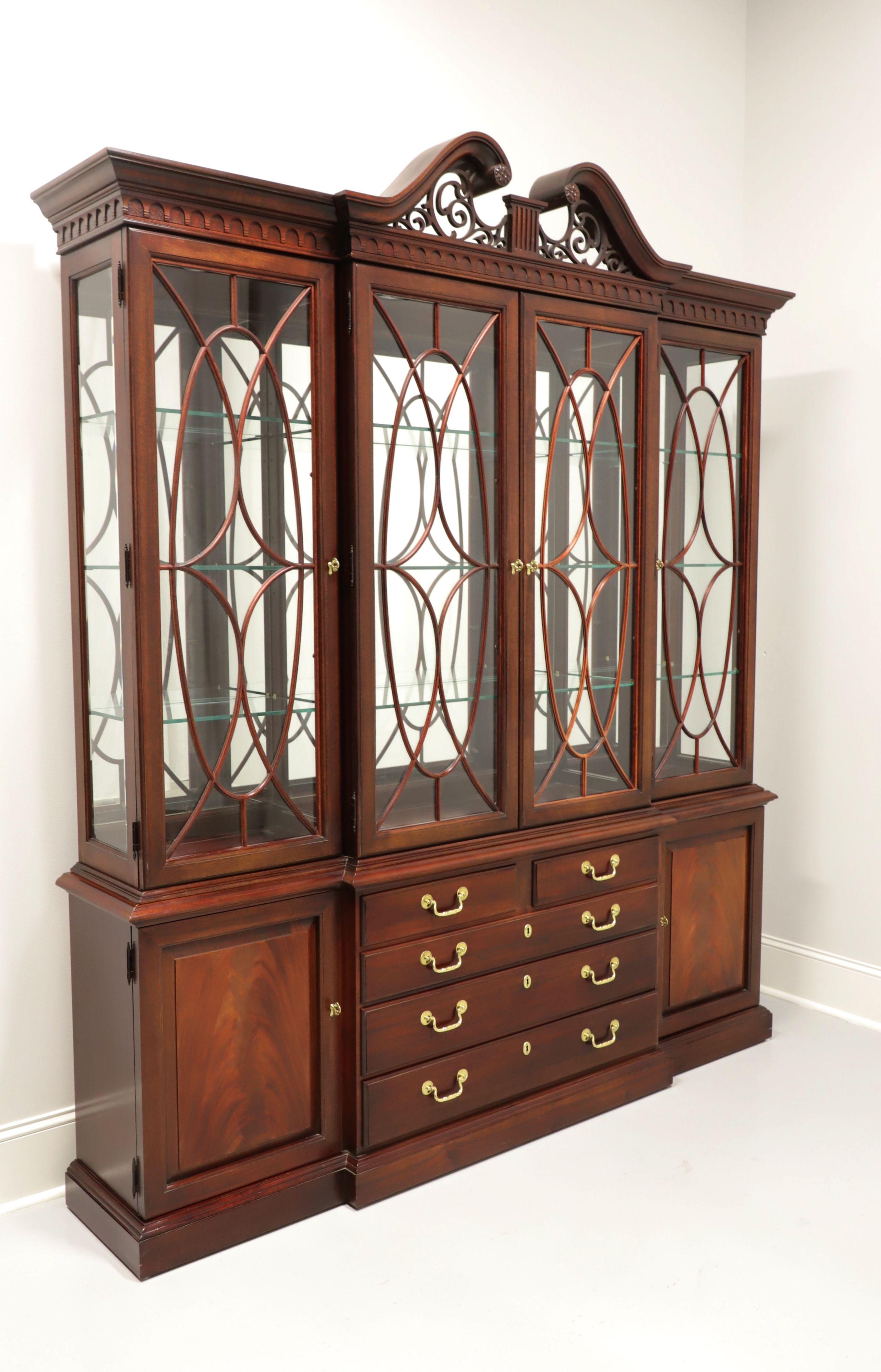 A Chippendale style breakfront china cabinet by Thomasville. Flame mahogany, brass hardware, top finished with crown & dentil molding and a center fretwork scroll pediment. Upper cabinet features three lighted compartments with three adjustable