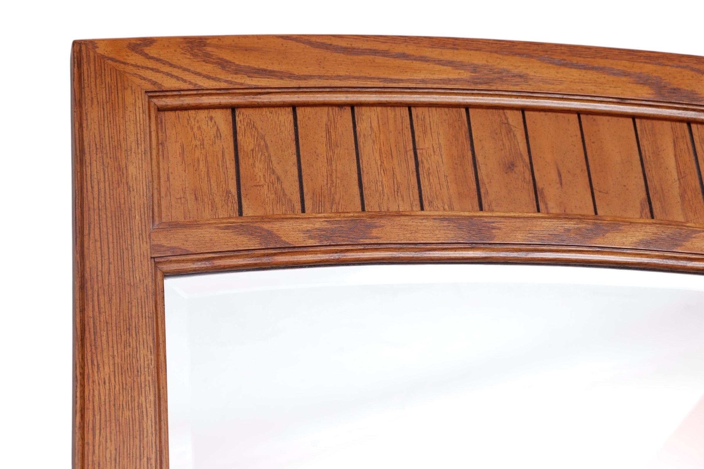 Miroir vertical de style mid-century fabriqué par Thomasville. Un simple cadre en chêne est décoré sur le dessus d'un panneau encastré qui donne l'impression d'un arc segmenté. Cet arc légèrement incurvé est suivi par le biseau du verre miroir. Une