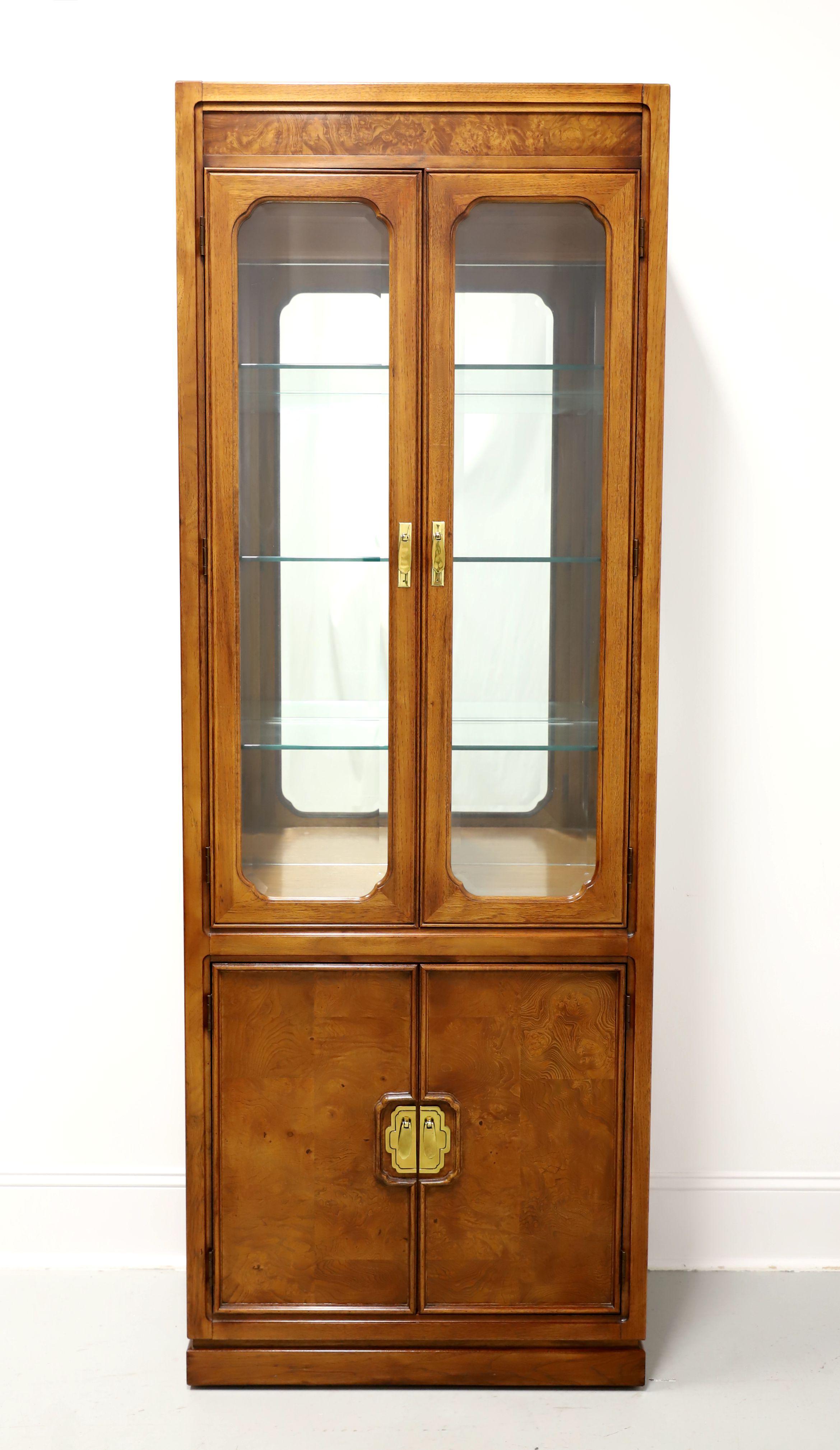 An Asian inspired curio display cabinet by Thomasville, from their Mystique Collection. Walnut with inlaid burl walnut at top & lower door panels, decorative brass hardware, and a solid base. Upper lighted cabinet features dual beveled glass doors,
