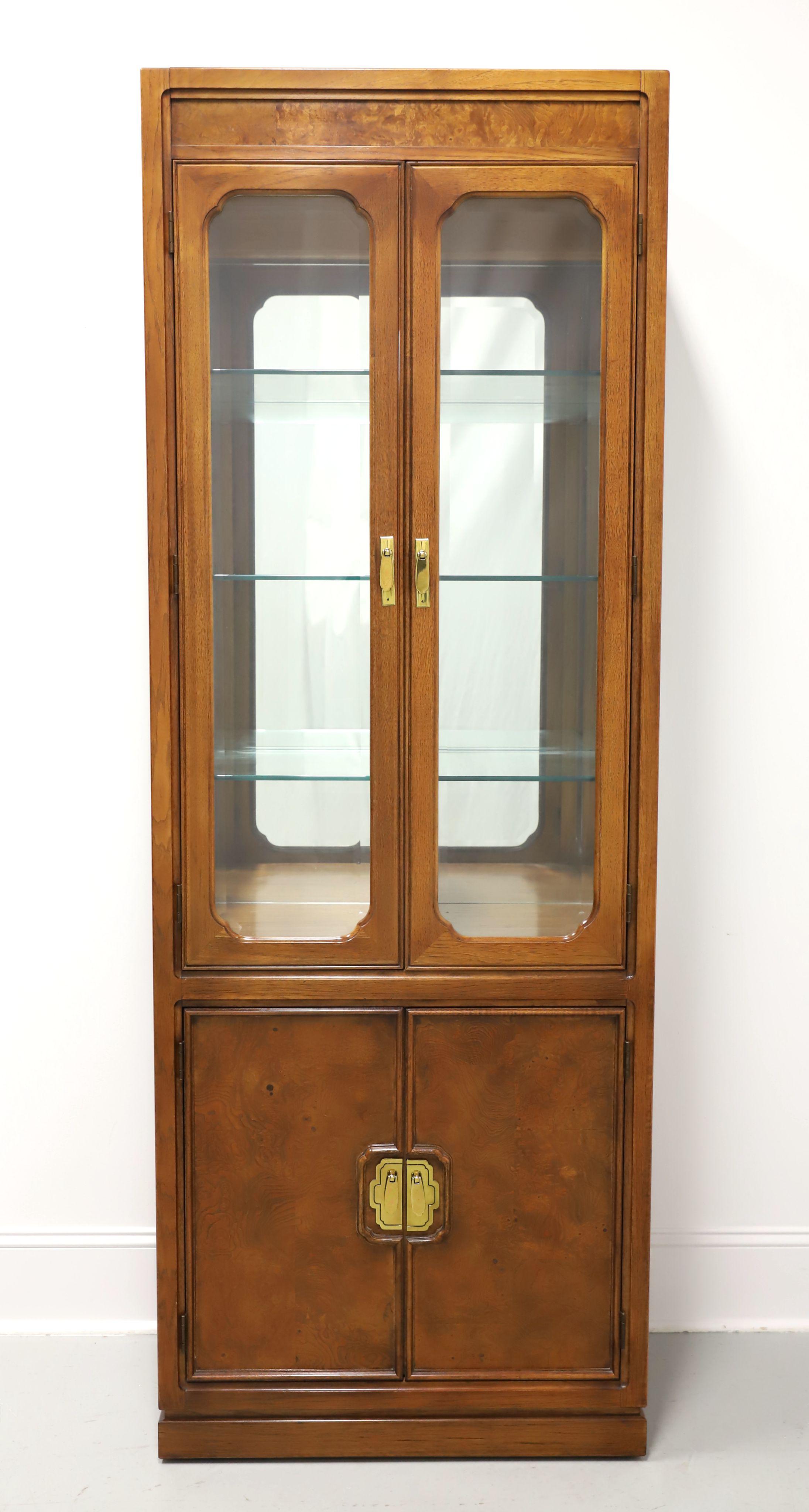 An Asian inspired curio display cabinet by Thomasville, from their Mystique Collection. Walnut with inlaid burl walnut at top & lower door panels, decorative brass hardware, and a solid base. Upper lighted cabinet features dual beveled glass doors,