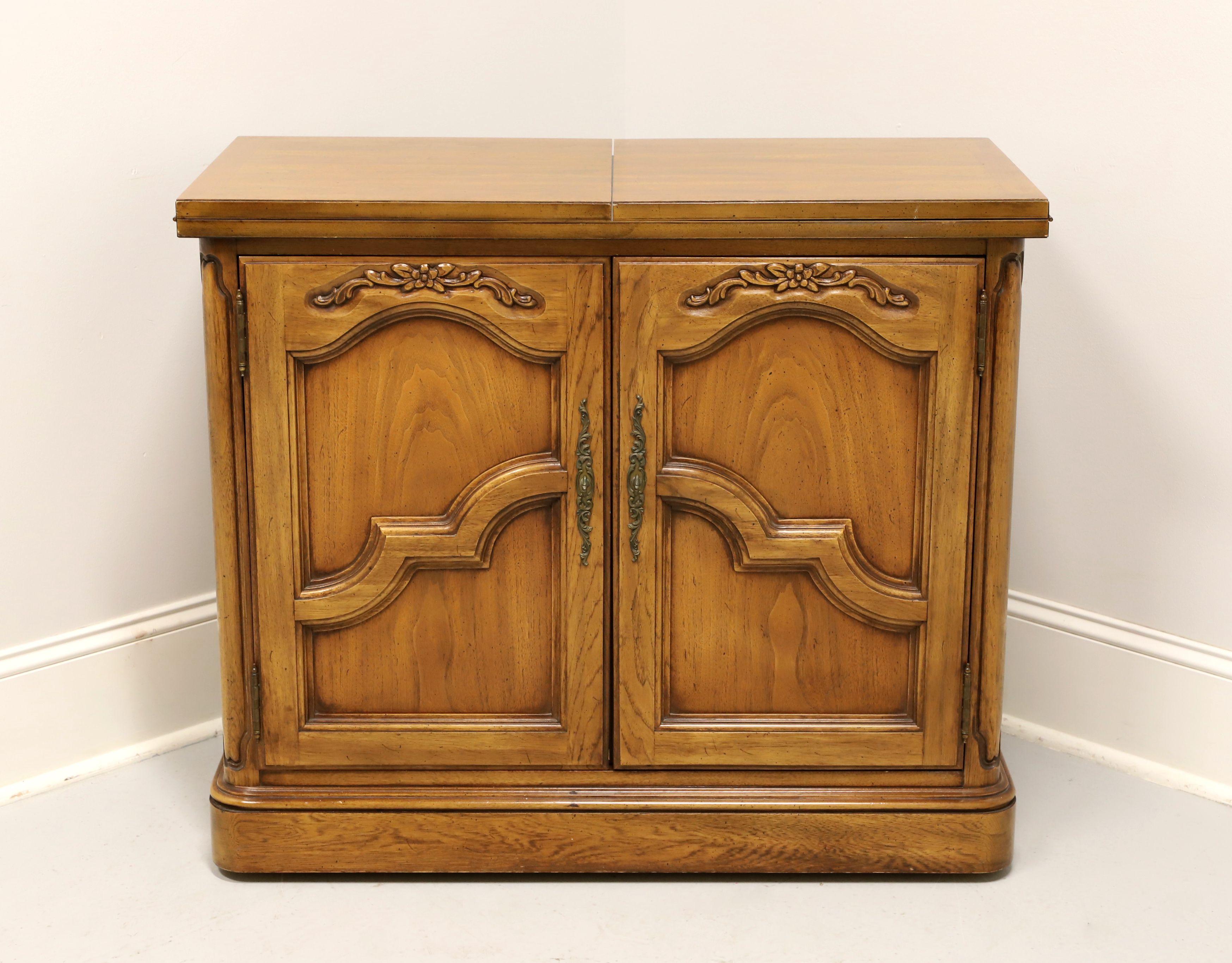 A French Country server by Thomasville. Solid oak with banded top, decorative carvings to door fronts, brass hardware, flip out hard composite surface expanded top and on wheels for easy movement. Features the flip out top exposing the composite