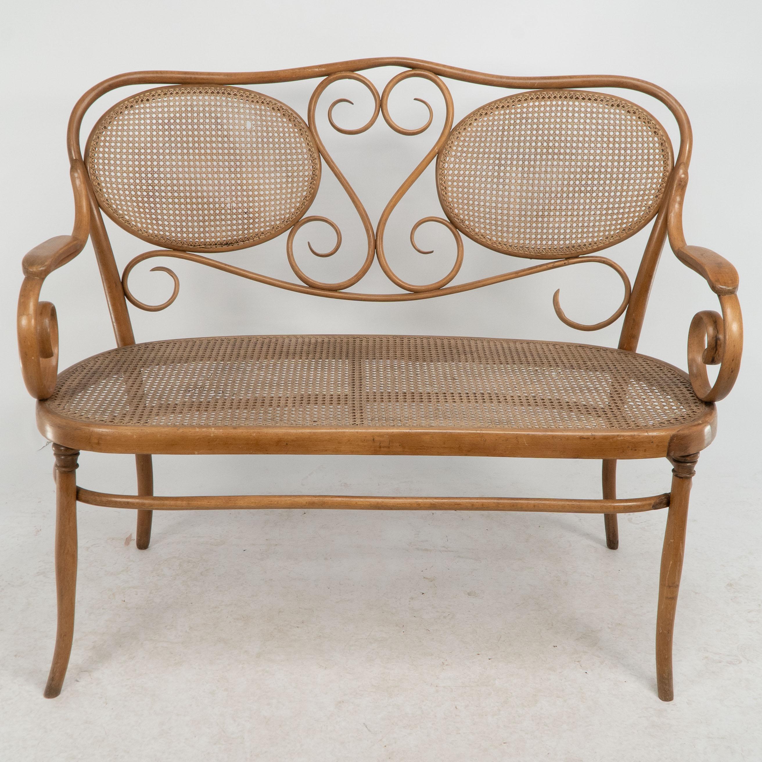 Thonet.
A bentwood Beech settee with wonderful scrollwork decoration to the back and to the arms with a caned seat and a caned back.