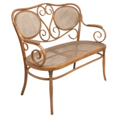 Antique Thonet. A bentwood settee with scrollwork decoration with caned seat & back