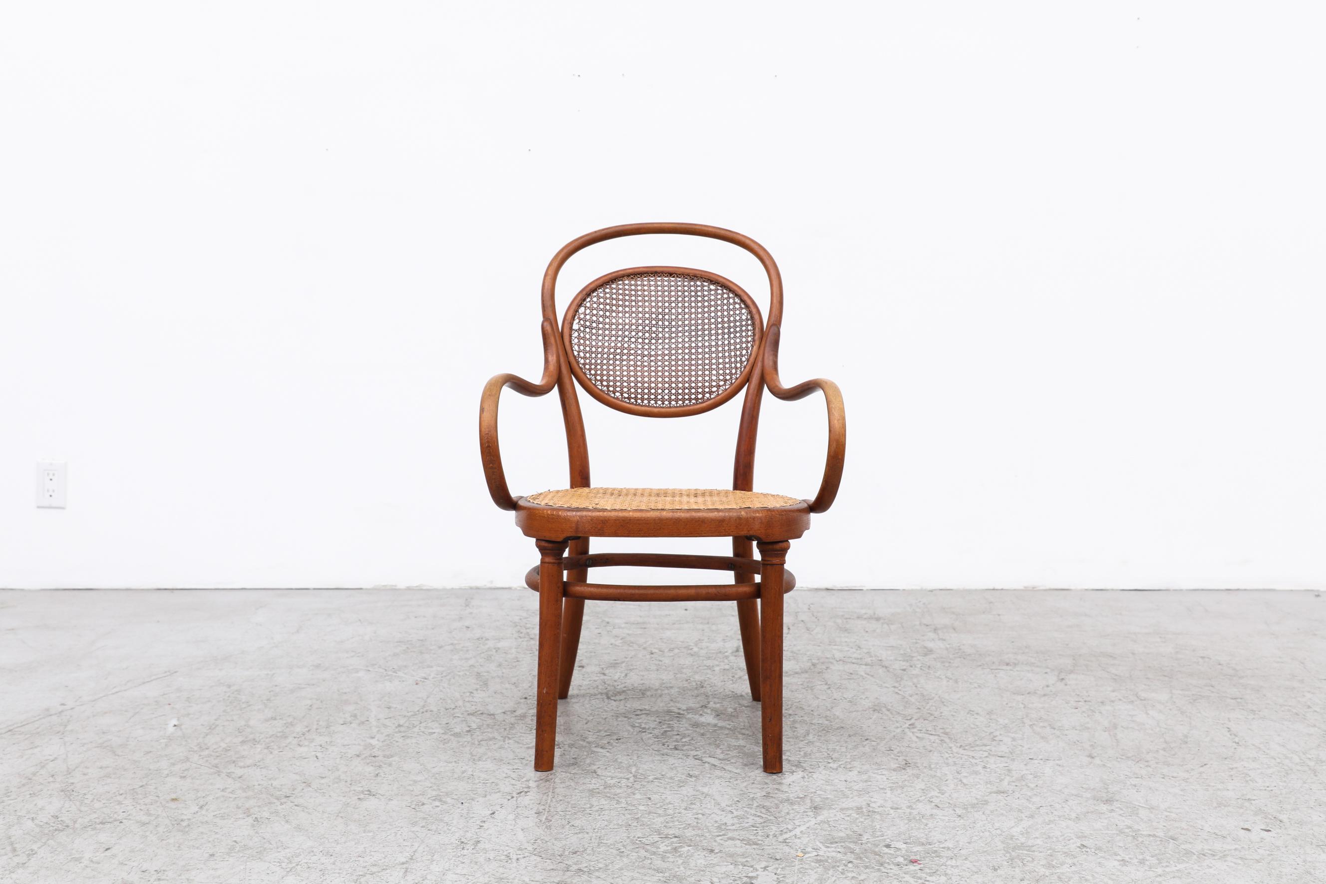 Rare and antique Thonet armchair with cane seating and bentwood armrests. This chair is at least 104 years old and was made between 1891 and 1919. It is in original condition with some visible patina and wear including loose and fraying cane on the