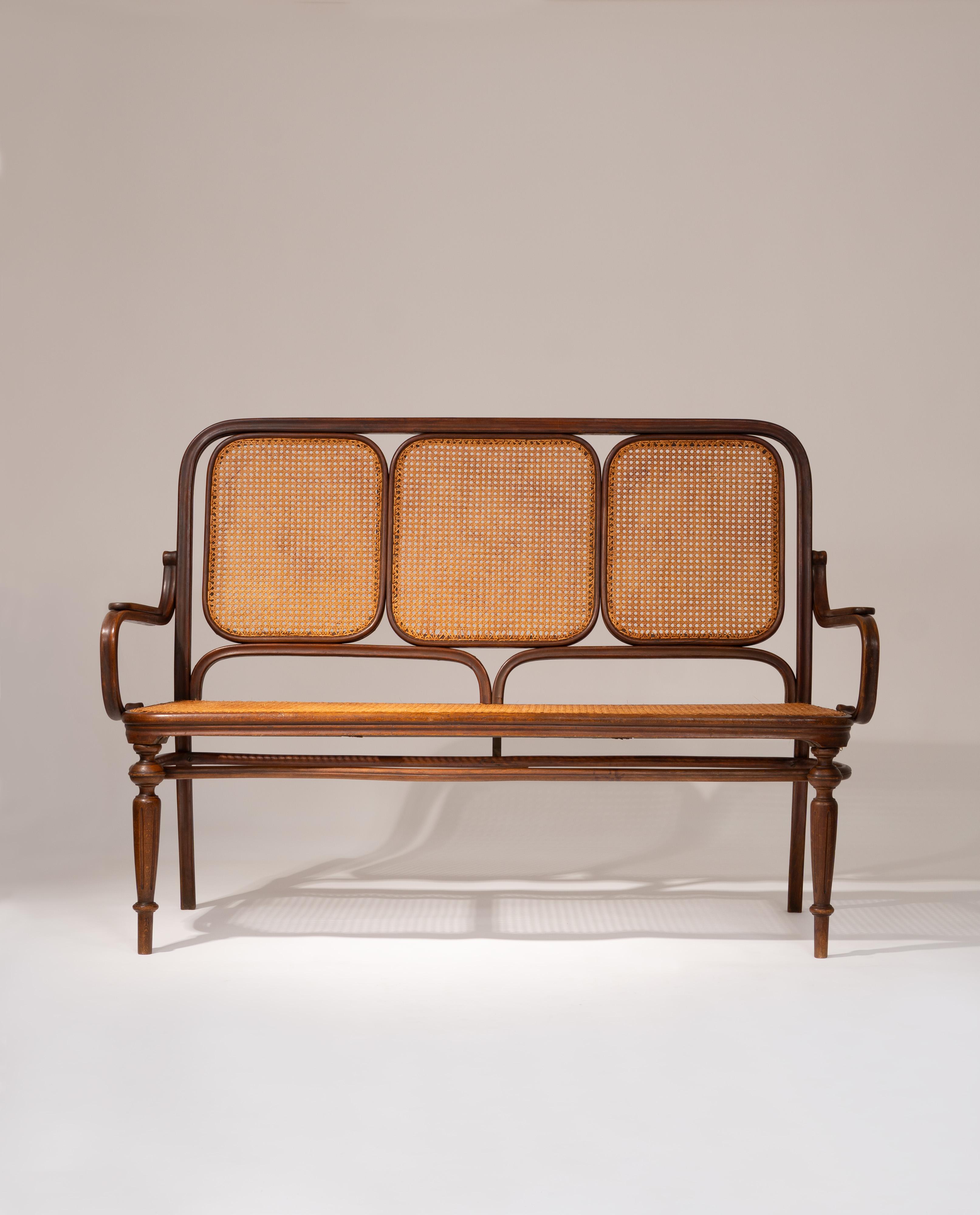 This late 19th-century Thonet bench showcases the elegance and innovation of Michael Thonet’s iconic bentwood furniture designs. Crafted with a bentwood frame, the bench features the distinctive curves and fluid lines that define Thonet’s masterful