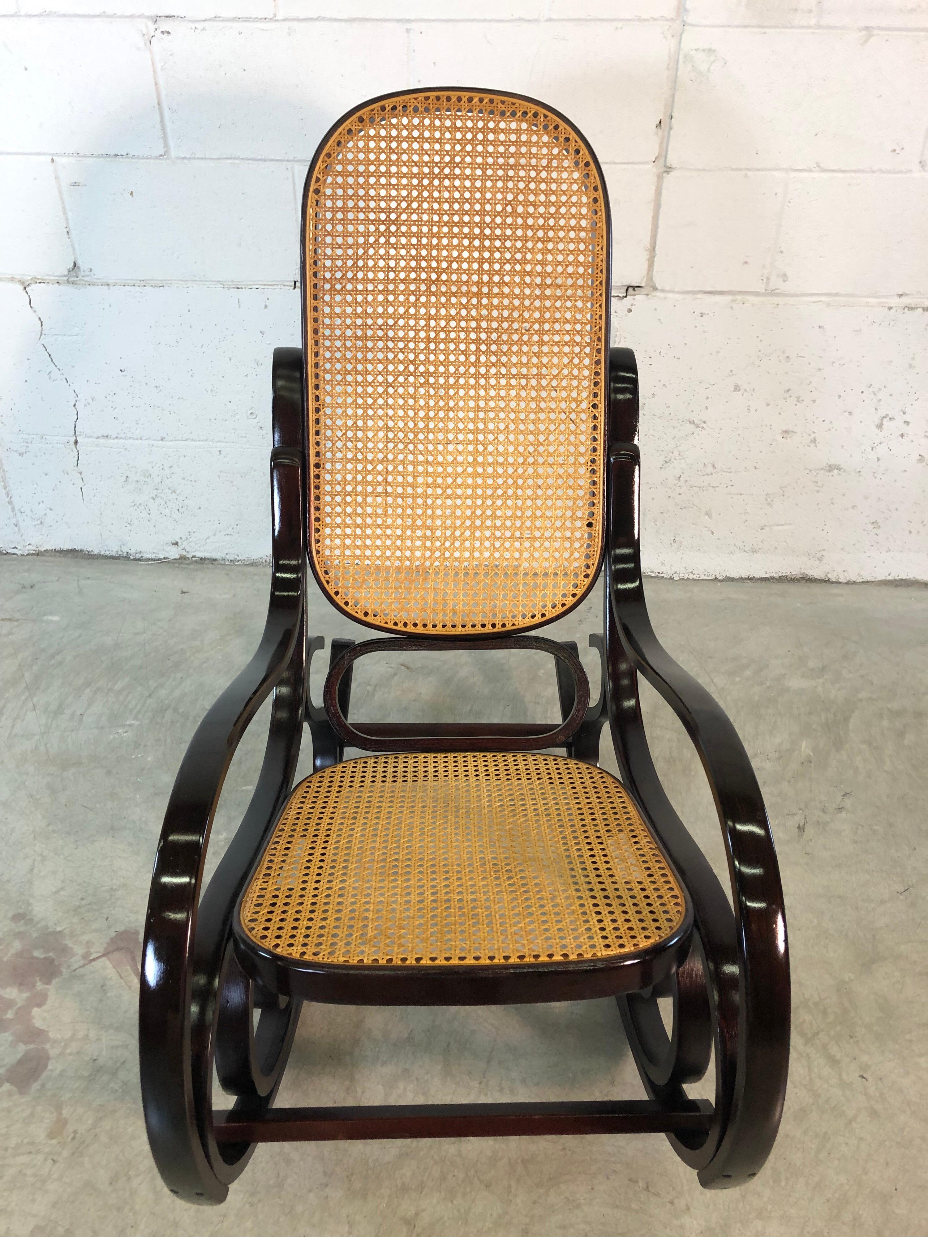 1970s dark brown wood Thonet style rocking chair with caned seat and back. The rocking chair has been completely refinished and restored and is in excellent condition.