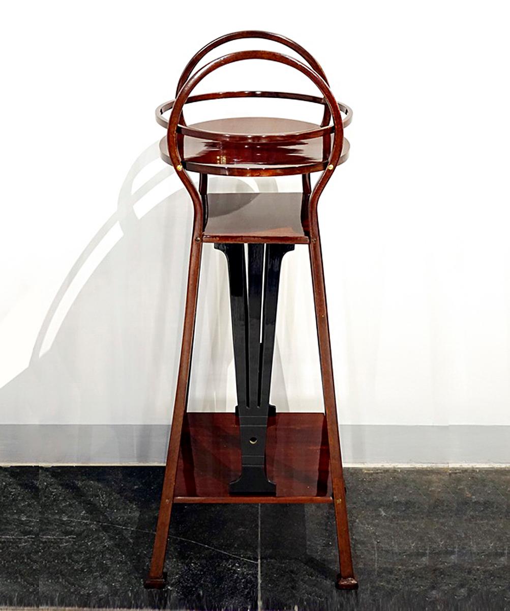 Pedestal with elegantly curved bentwood elements: four legs over a square plan, conically converging upwards, protruding at the top end, whereby two legs are connected to each other by a circular bend, within this headpart a circular shelf with a