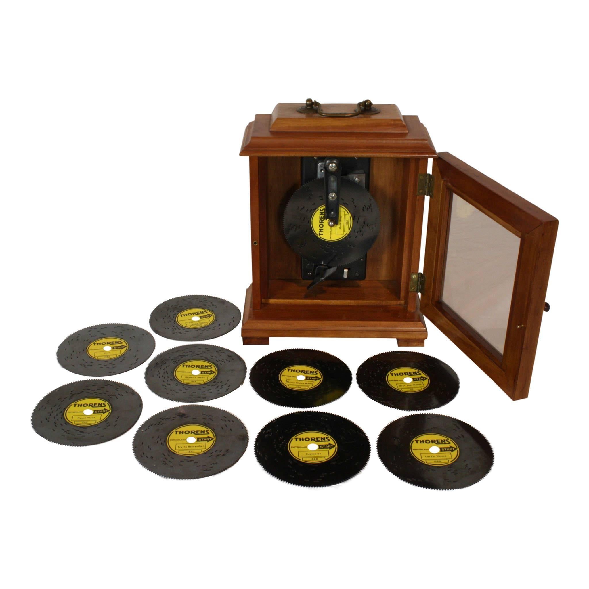 A quality fruitwood case with a glass door allows for viewing the metal discs that play on this upright music box by Thorens of Switzerland. The set includes ten discs, titled: Try to Remember, Over the Waves, More, Lara's Theme, Moon River, Faust