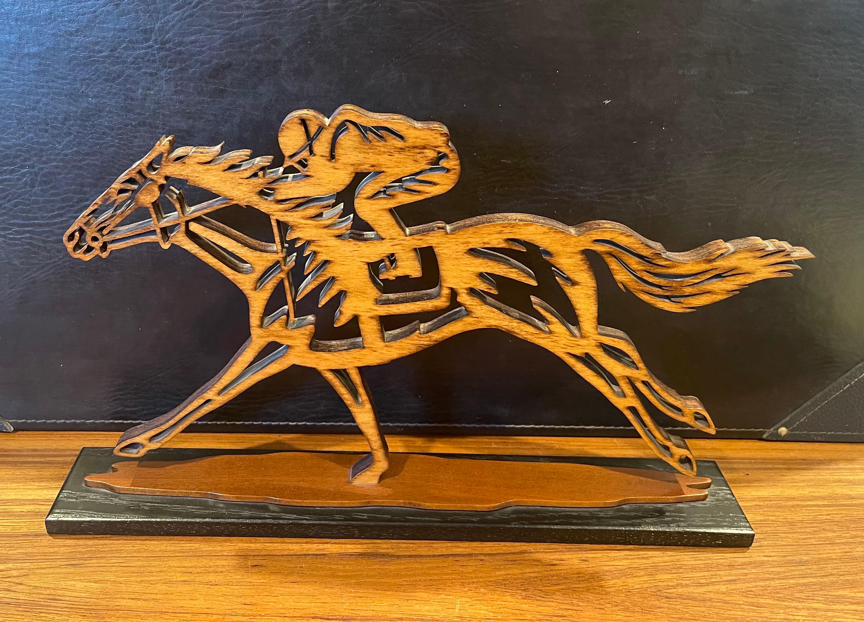 Wonderful carved wood sculpture of a thoroughbred horses racing with jockey aboard, circa 1990s. Great detail and patina on wood base! The piece is in very good condition and measures 2.5
