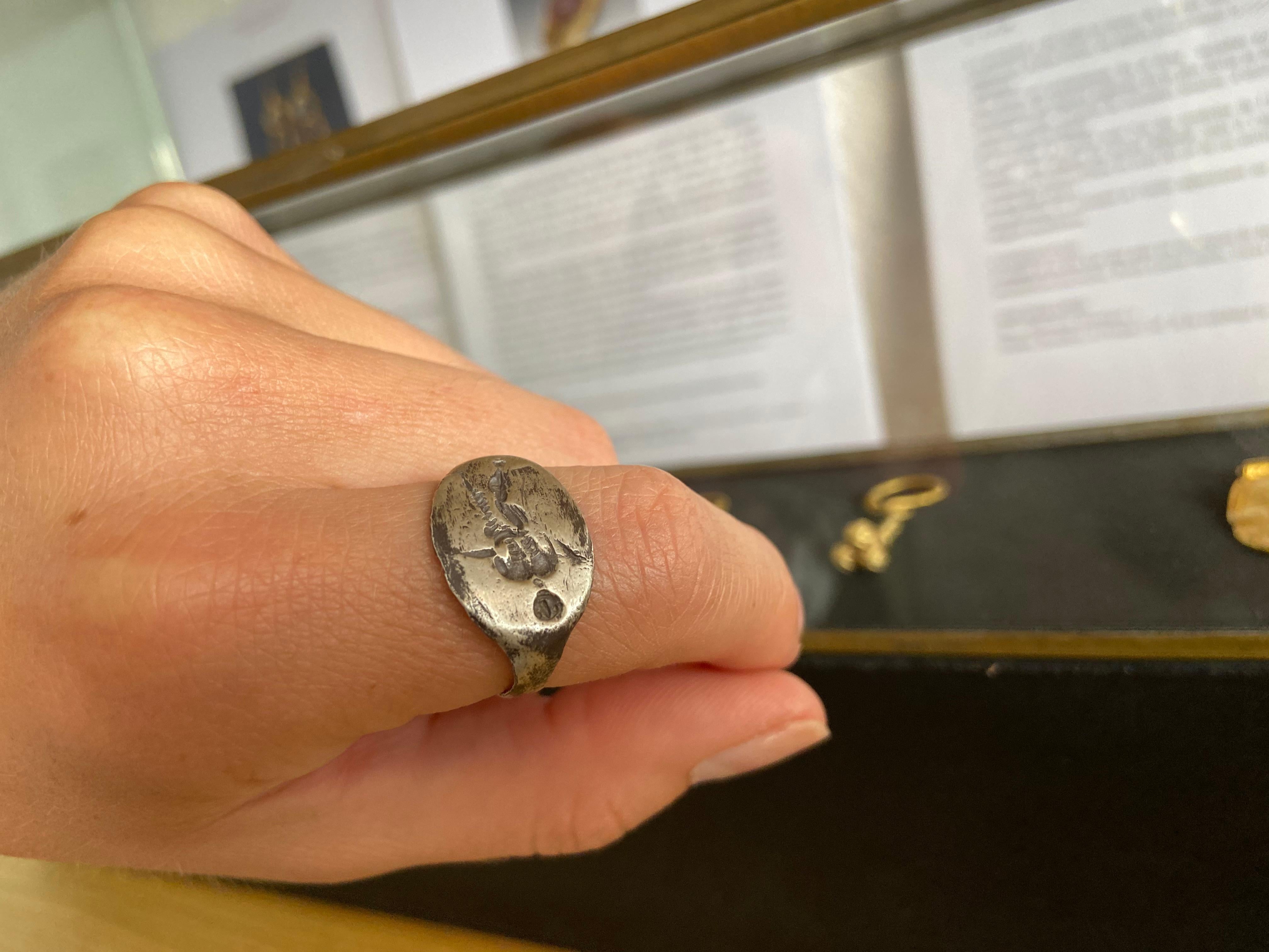 A silver ring with D-section hoop, flat discoid bezel with a nude male figure with stylized facial features, standing behind branches. 3.67 grams, measures: 22.62mm overall, 20.68mm internal diameter (approximate size British R, USA 8 1/2, Europe 18