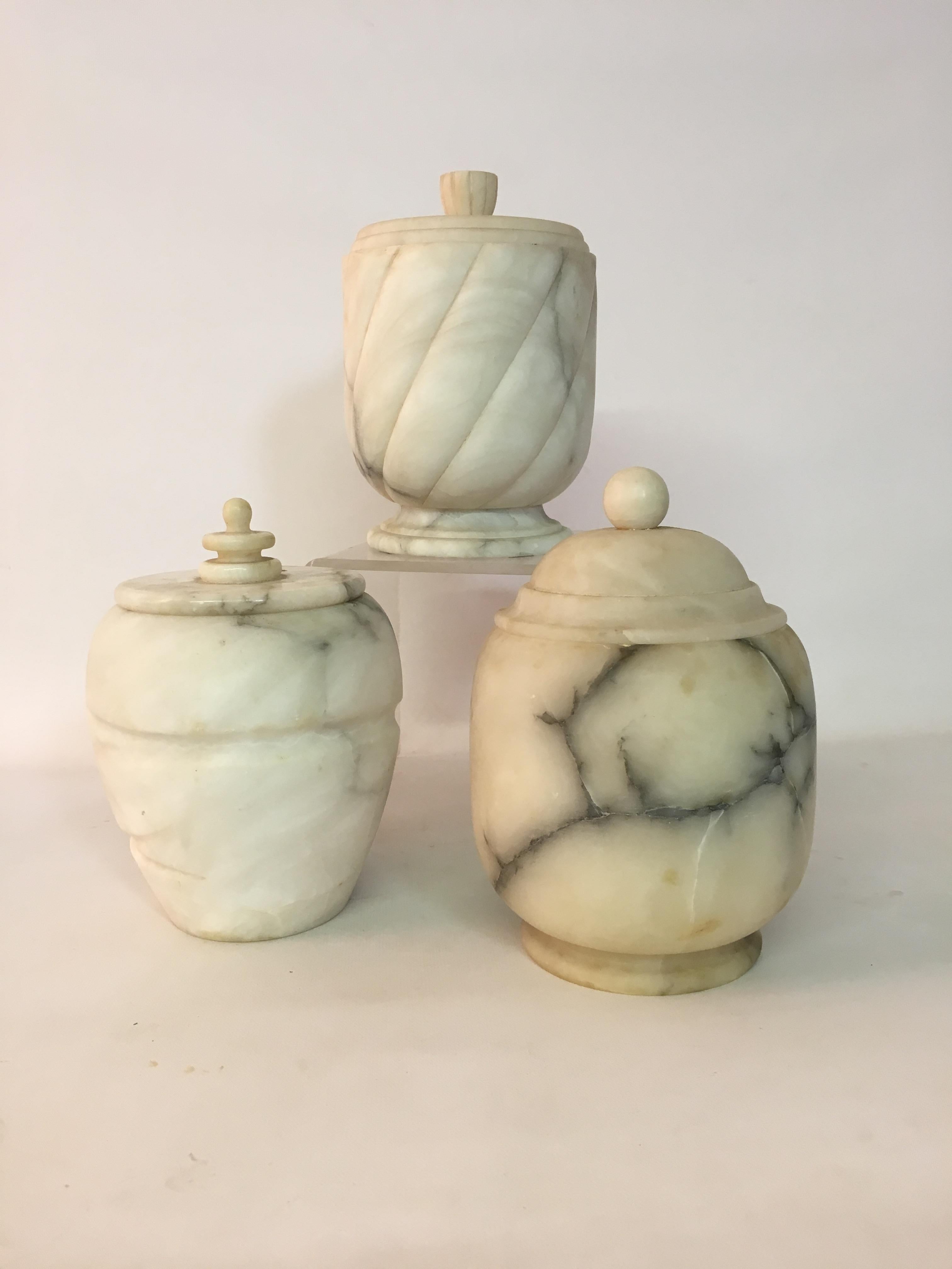 Three uniquely carved white Carrara, Italian marble canisters with gray/black veining. Purchased in the 1950s and lovingly cared for and admired. Wonderful storage.

The dimensions range from 7.75
