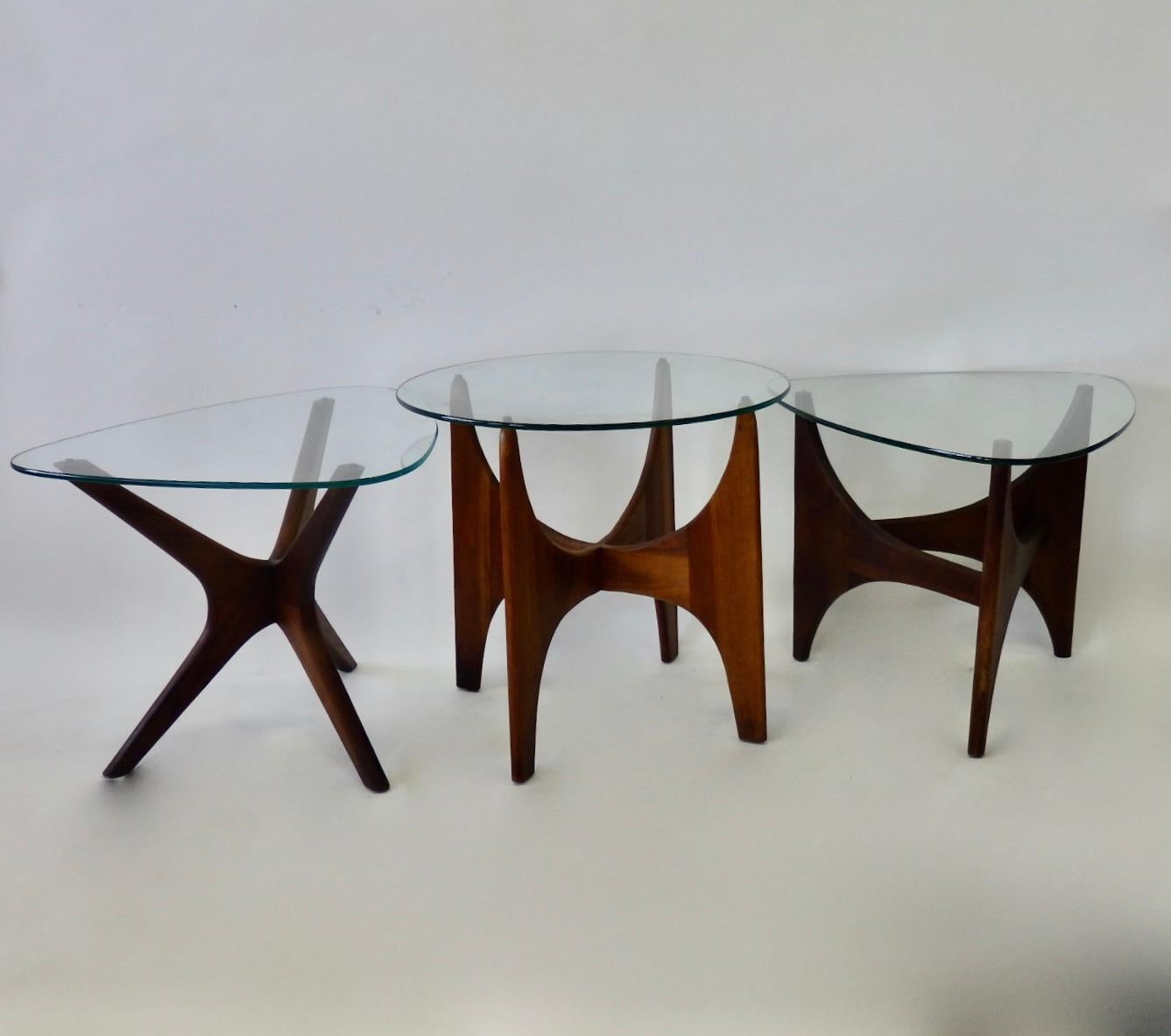 Selection of three separate Adrian Pearsall designed side tables. Each with walnut base and glass top. Two have guitar pick shaped tops. Third holds round glass top. Guitar pick tops measure 23.88 wide - 27 deep - 19.5 tall . Round table measures 24