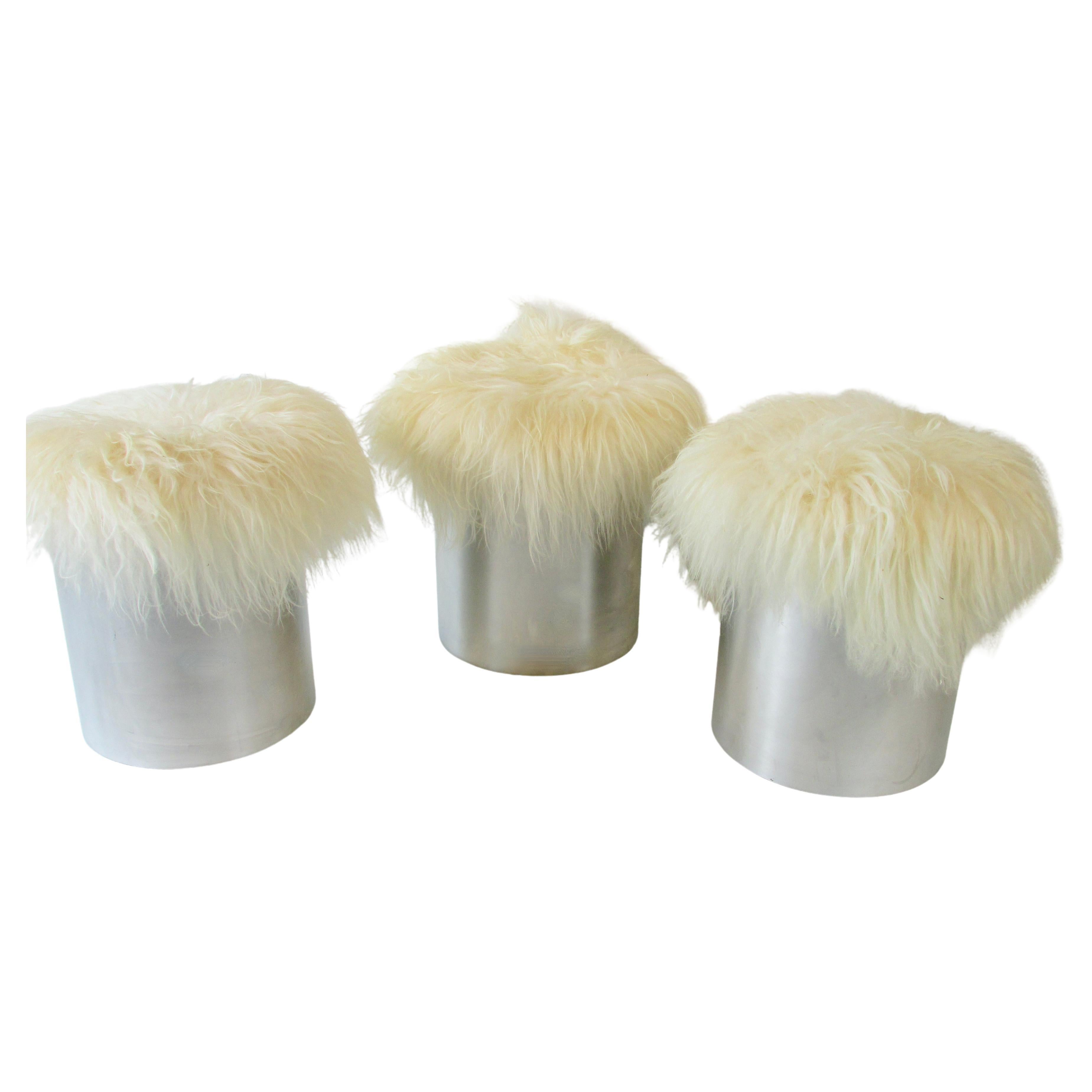 Three welded seam cylinder base stools or ottomans with curly lamb covering . Made in England label on the underside . Clean originals some scuffs on bases .