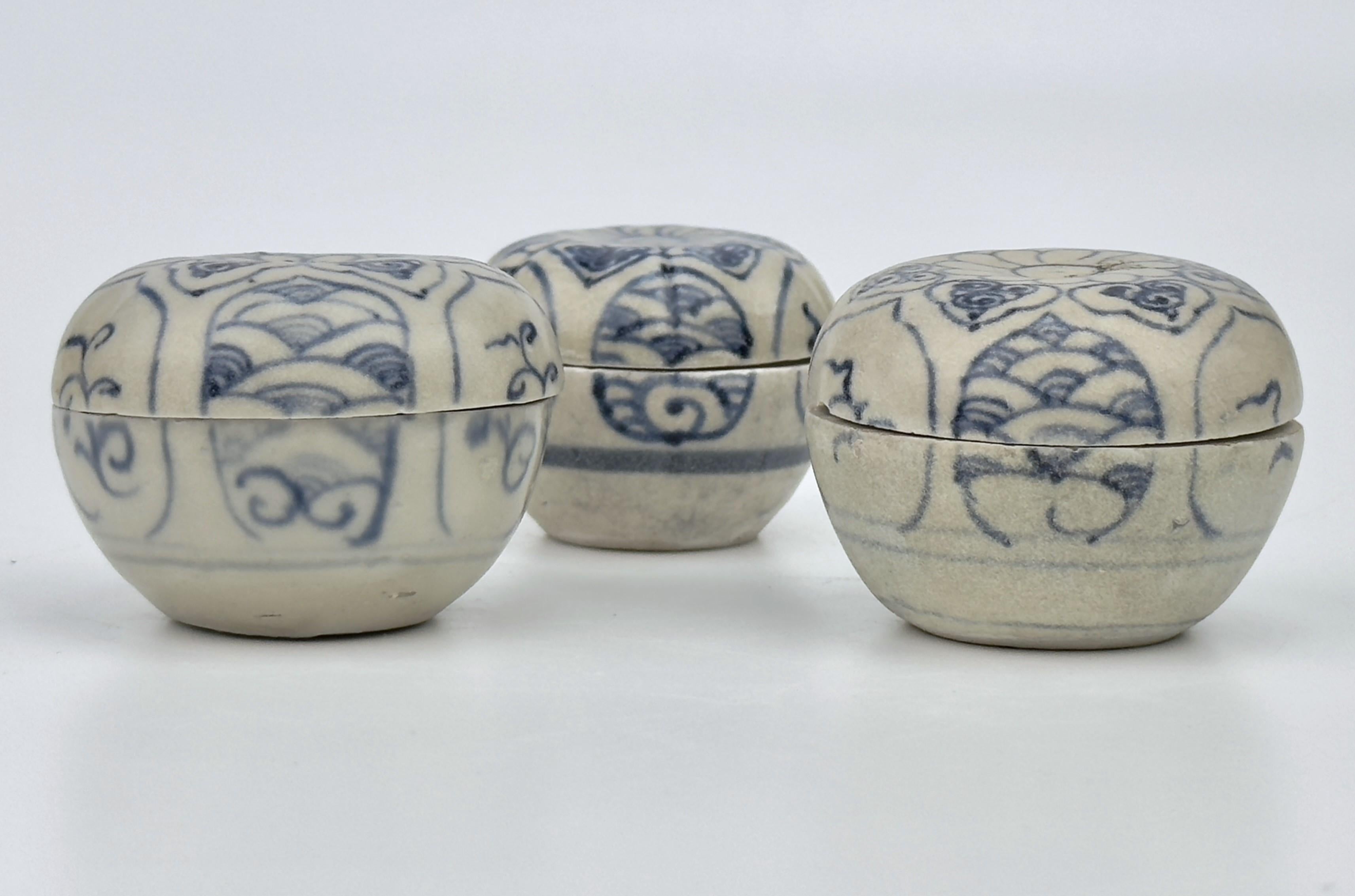 Se trata de tres pequeñas cajas con tapa de la época vietnamita, concretamente del siglo XV, durante la dinastía Le. Cada caja presenta intrincados diseños florales en azul sobre fondo blanco. Las cajas son redondas con tapas abovedadas, y los