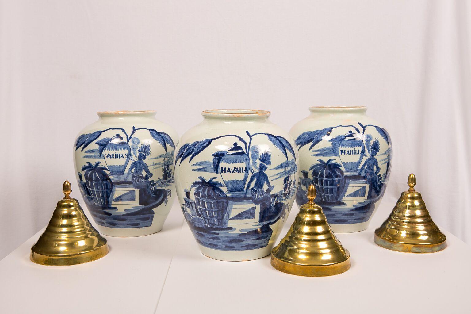 A set of three blue and white Dutch delft tobacco jars with brass covers each painted on the front with a Native American chieftain smoking a pipe. Each jar is inscribed with the locale from which the tobacco originated: 