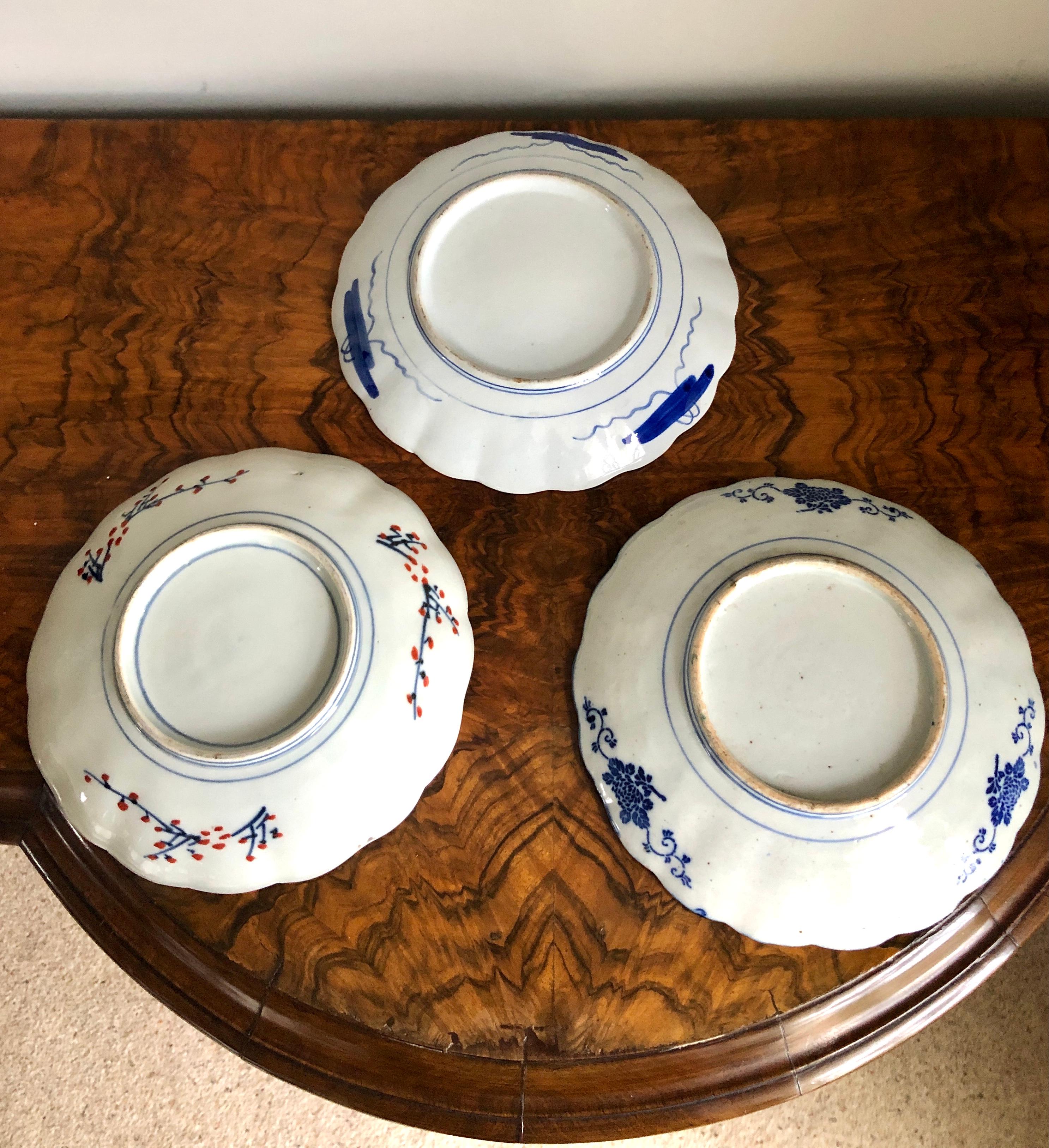 A set of three Imari Japanese plates all being very vibrant and prettilly hand painted with scenes of flowers, leaves and goldfish in red, yellow, green, terracotta, blue and gold. They all boast scalloped edges with painted backs depicting