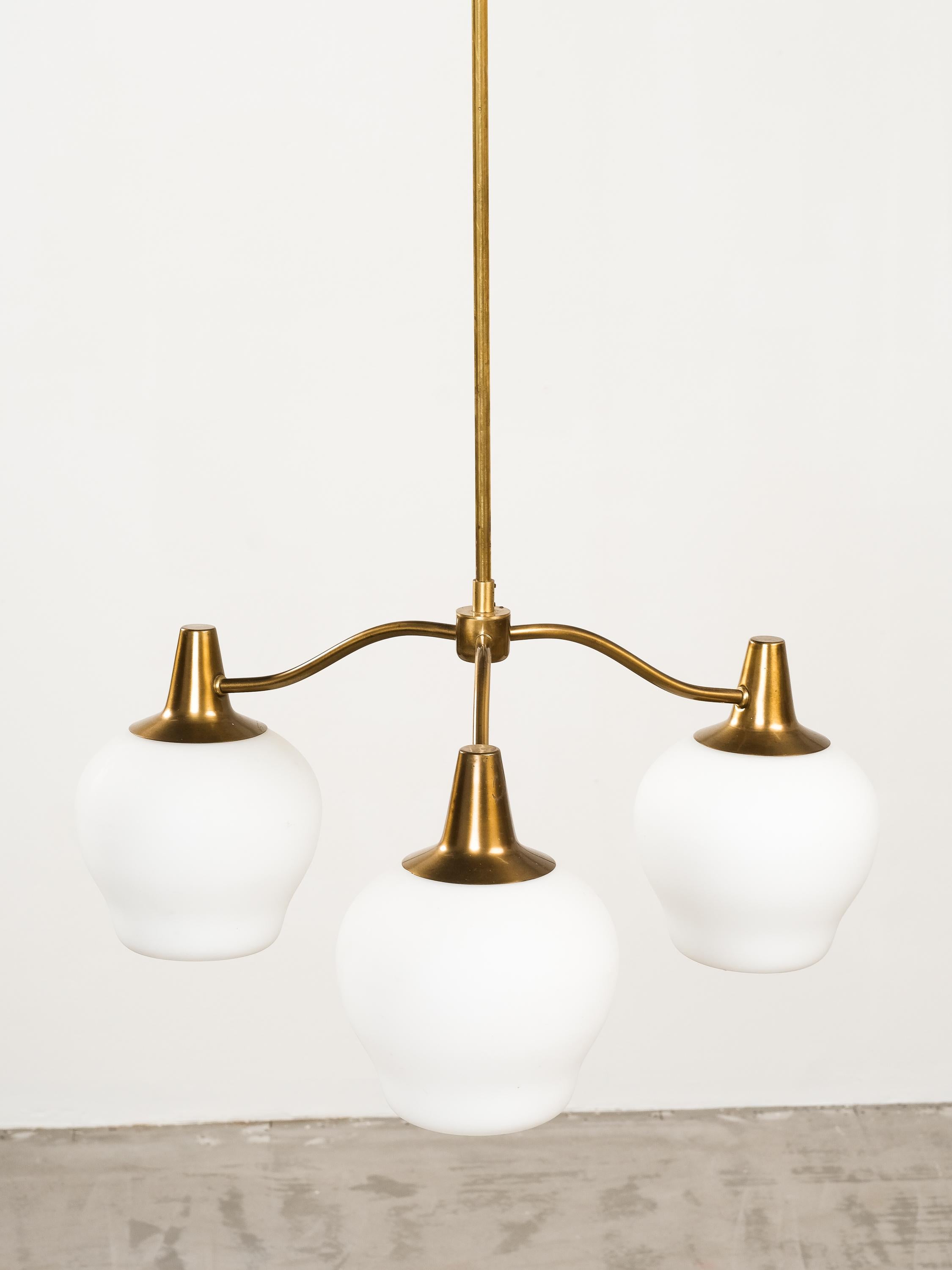 Questo raro lampadario a tre bracci è stato prodotto in Svezia nei primi anni Cinquanta. Stelo in ottone, tre bracci e accessori con paralumi in vetro opalino opaco. Un esempio di illuminazione moderna svedese molto suggestivo e semplicemente