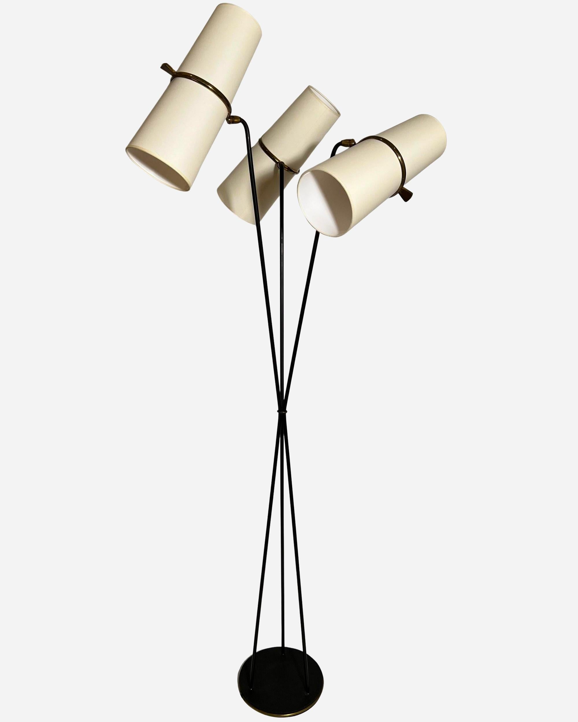 Lampada da terra in metallo laccato nero e ottone, composta da tre bracci luminosi in metallo laccato, tenuti insieme al centro da un anello in ottone e fissati a una base circolare in ghisa laccata nera con un angolo in ottone.
All'estremità di