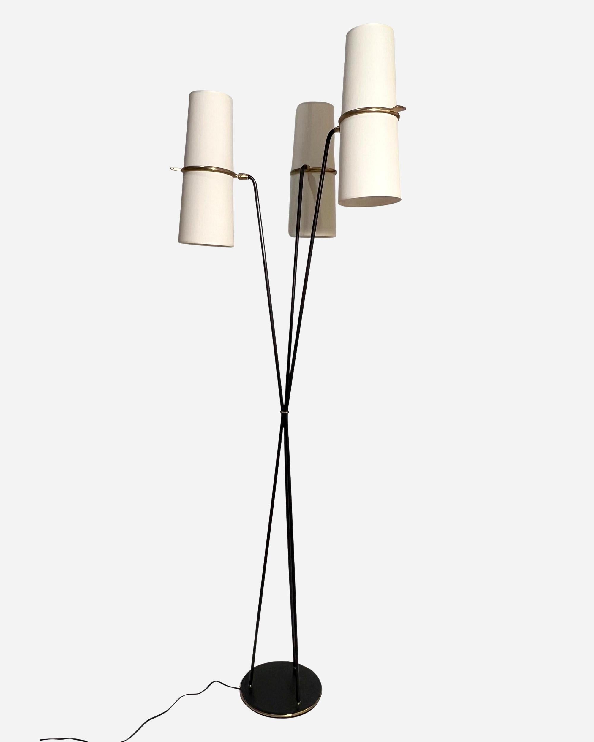 Floor lamp in black lacquered metal and brass, composed of three luminous lacquered metal arms, held together in the middle by a brass ring and fixed to a circular black-lacquered cast-iron base set with a brass angle.
At the end of each arm is a